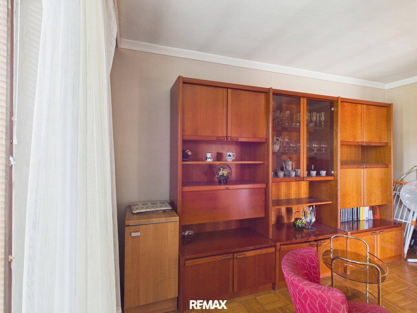 Wohnzimmer mit klassischen Holzschränken, Parkettboden und einem roten Sessel.