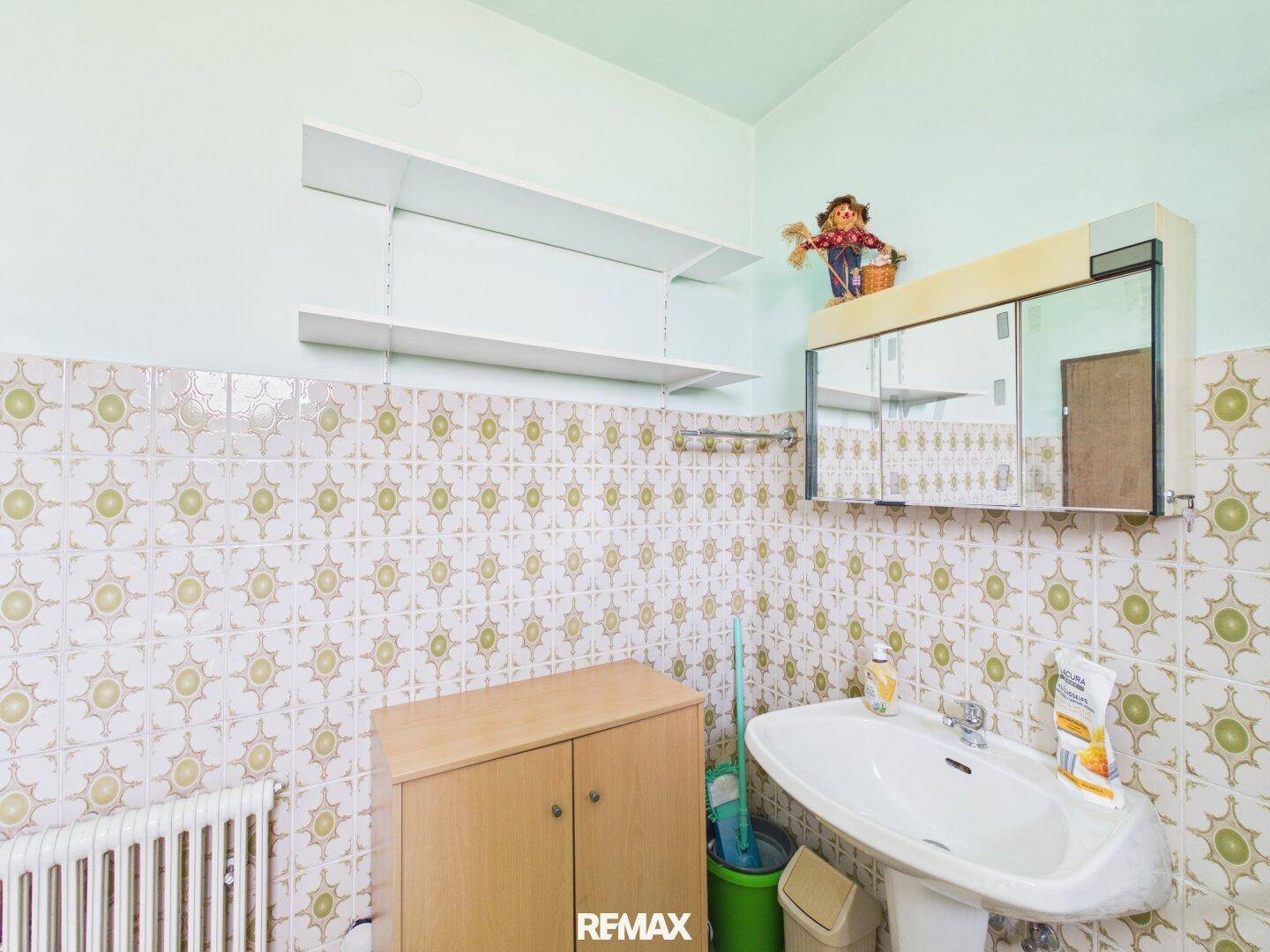 Badezimmer mit gemusterten Fliesen, Waschbecken und Spiegelschrank.
