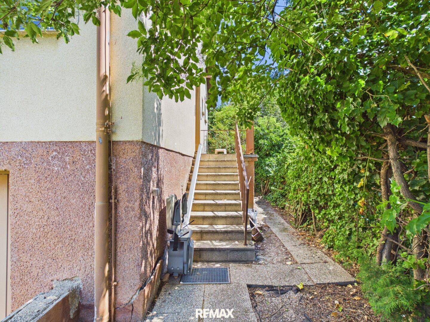 Außentreppe entlang des Hauses, umgeben von üppigem Grün.