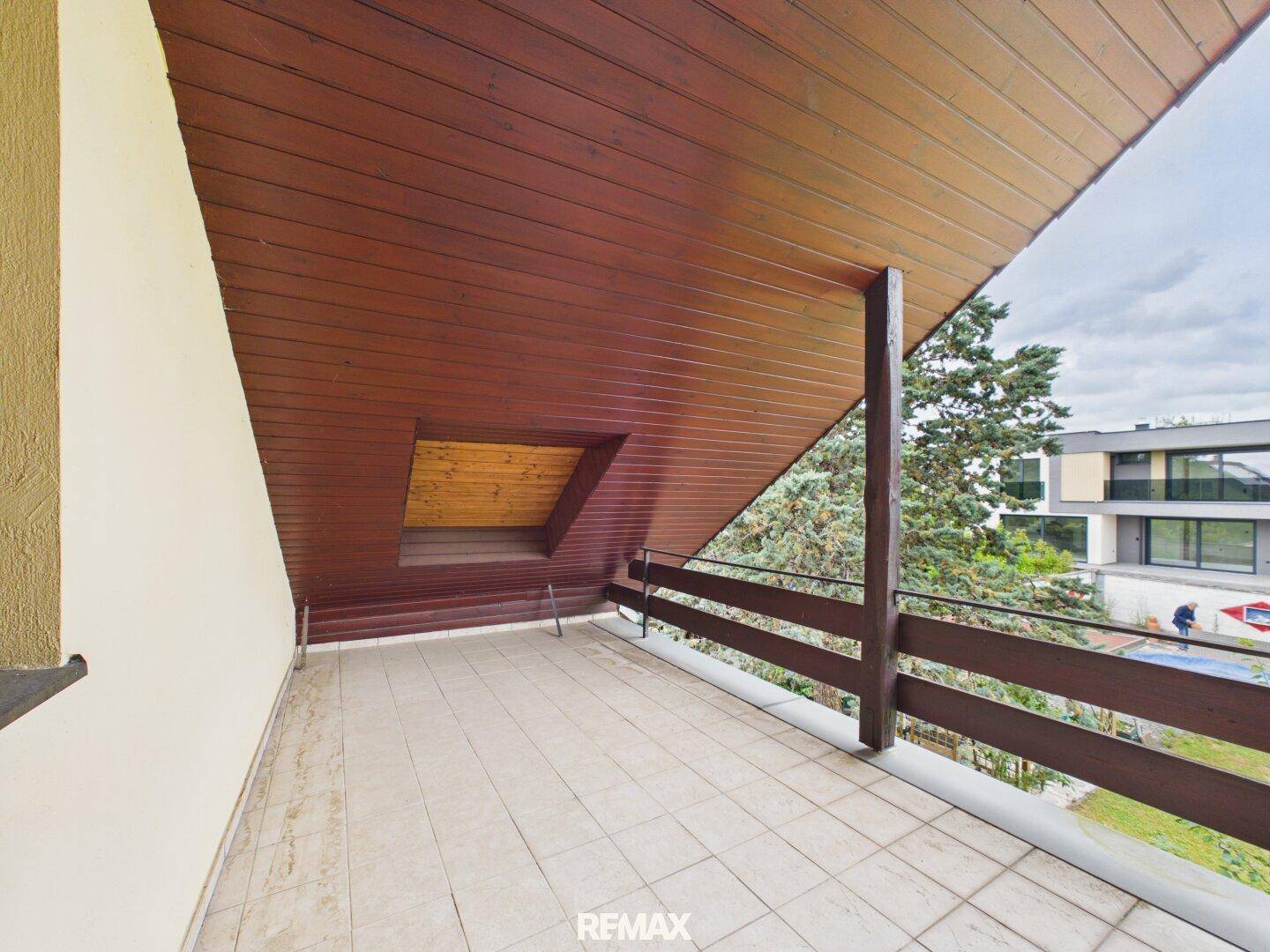 Überdachter Balkon mit Fliesenboden und Holzgeländer, ideal zum Entspannen im Freien.