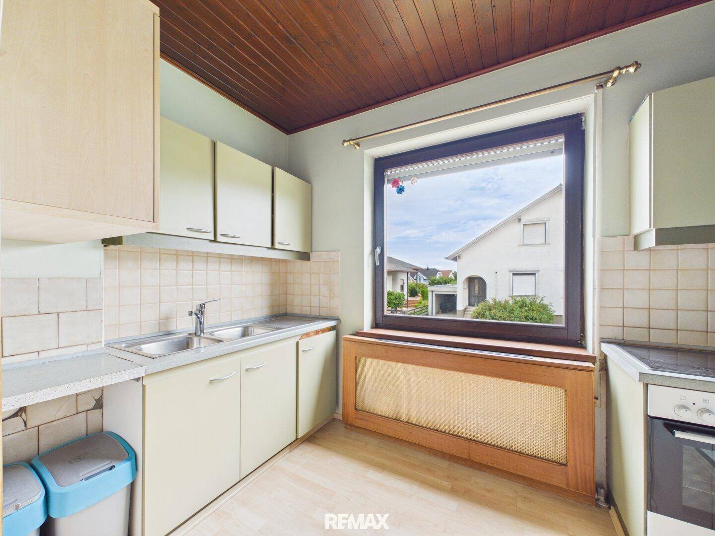 Funktionale Küche mit hellen Schränken, Fliesenrückwand und Fenster mit Blick ins Grüne.