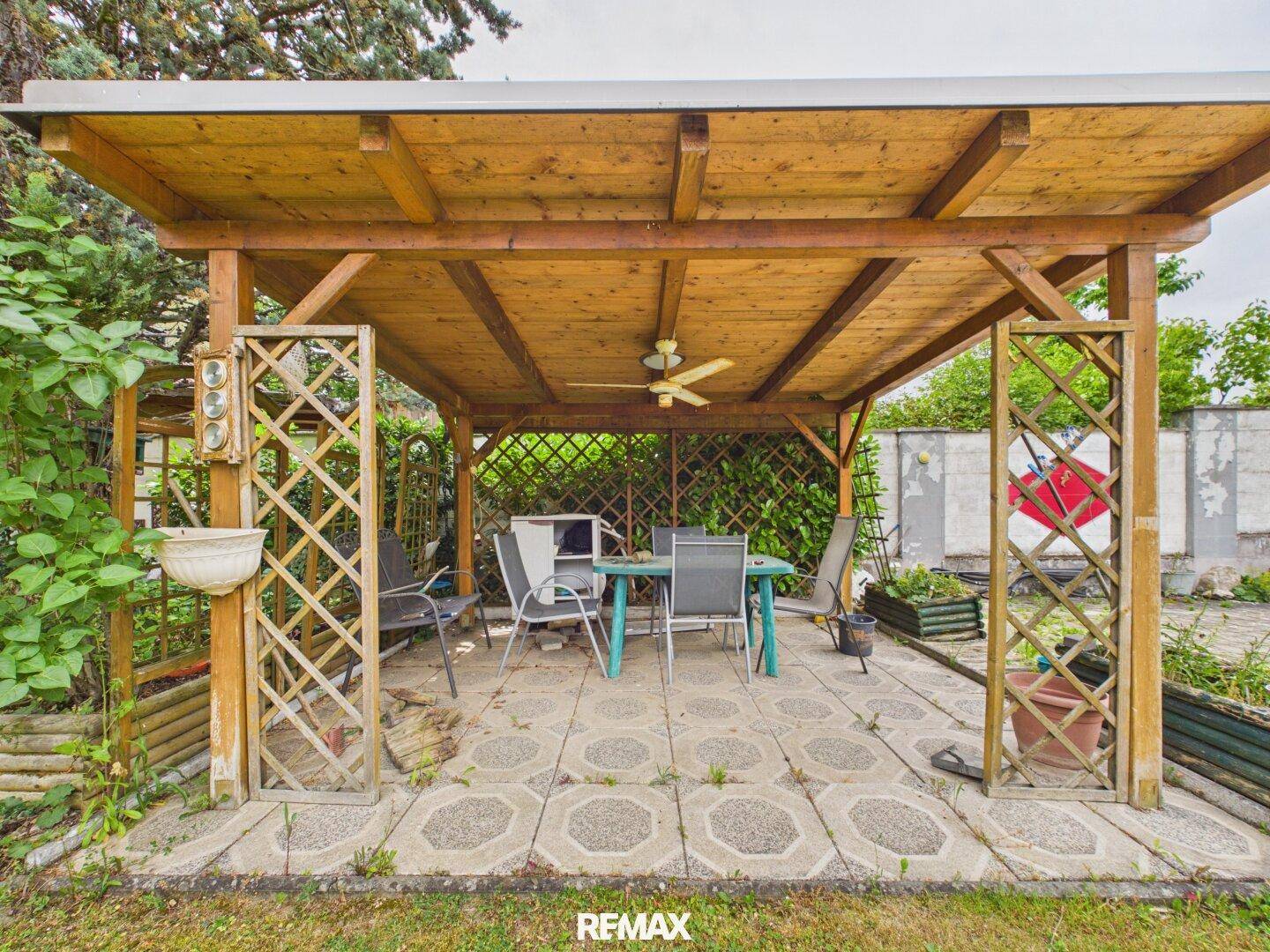Überdachte Terrasse im Garten mit Sitzgelegenheiten und Deckenventilator.