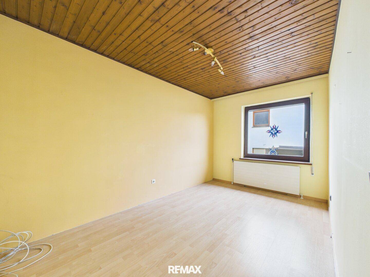 Geräumiges Schlafzimmer mit gelben Wänden, Holzboden und Holzdecke.