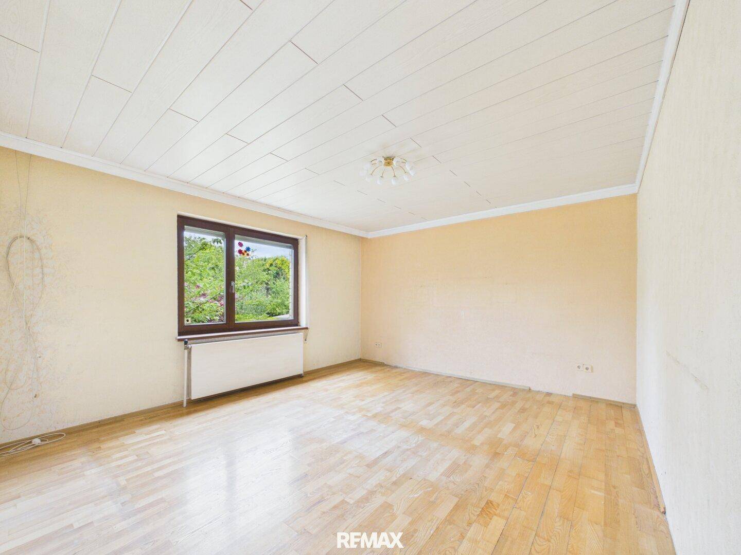 Helles Schlafzimmer mit Holzboden und Fenster mit Blick ins Grüne.