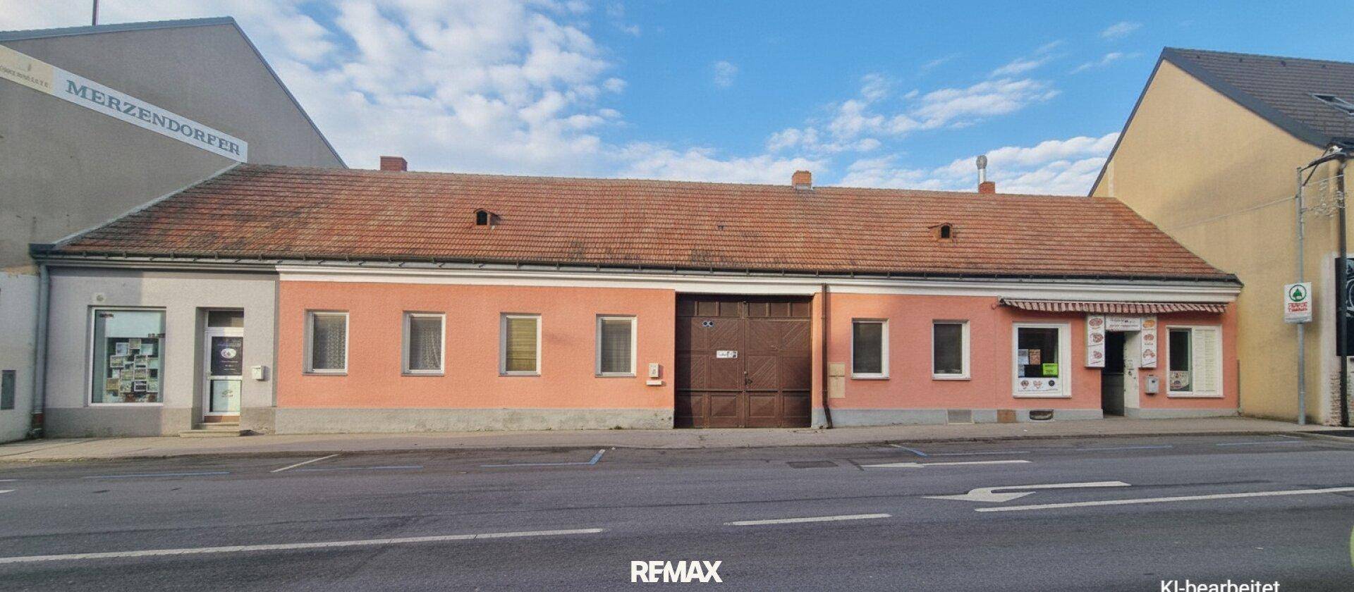 Lange rosa gestrichene Fassade eines Altbaus mit großem Holztor und kleinen Fenstern zur Straße.