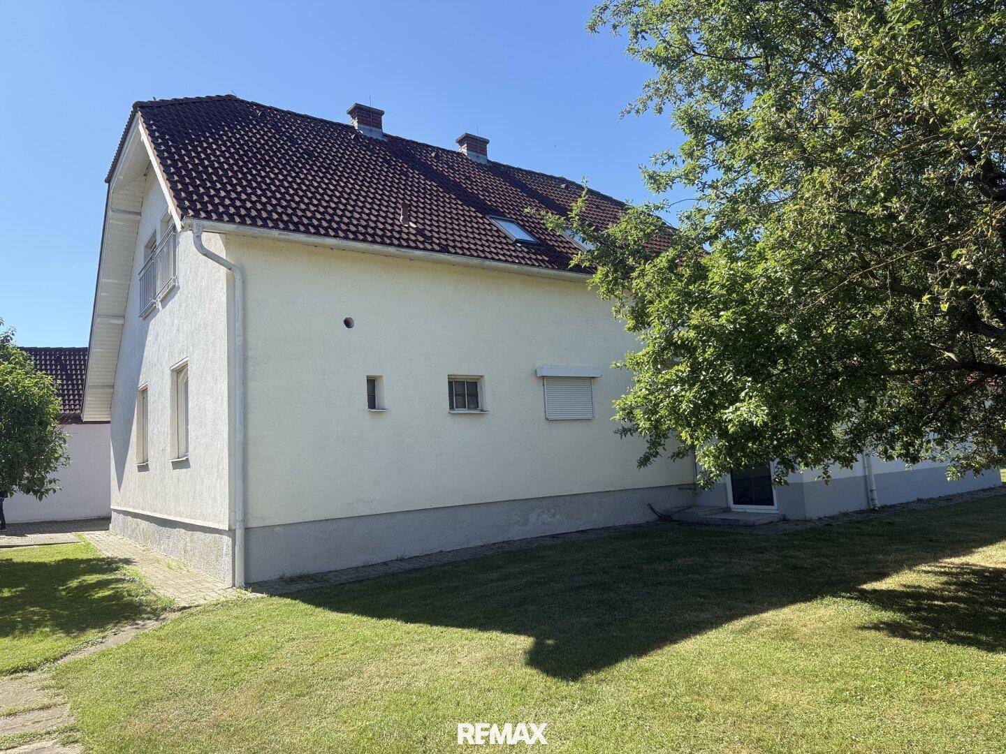 Seitenansicht des weißen Einfamilienhauses mit kleinen Fenstern und grünem Rasen.
