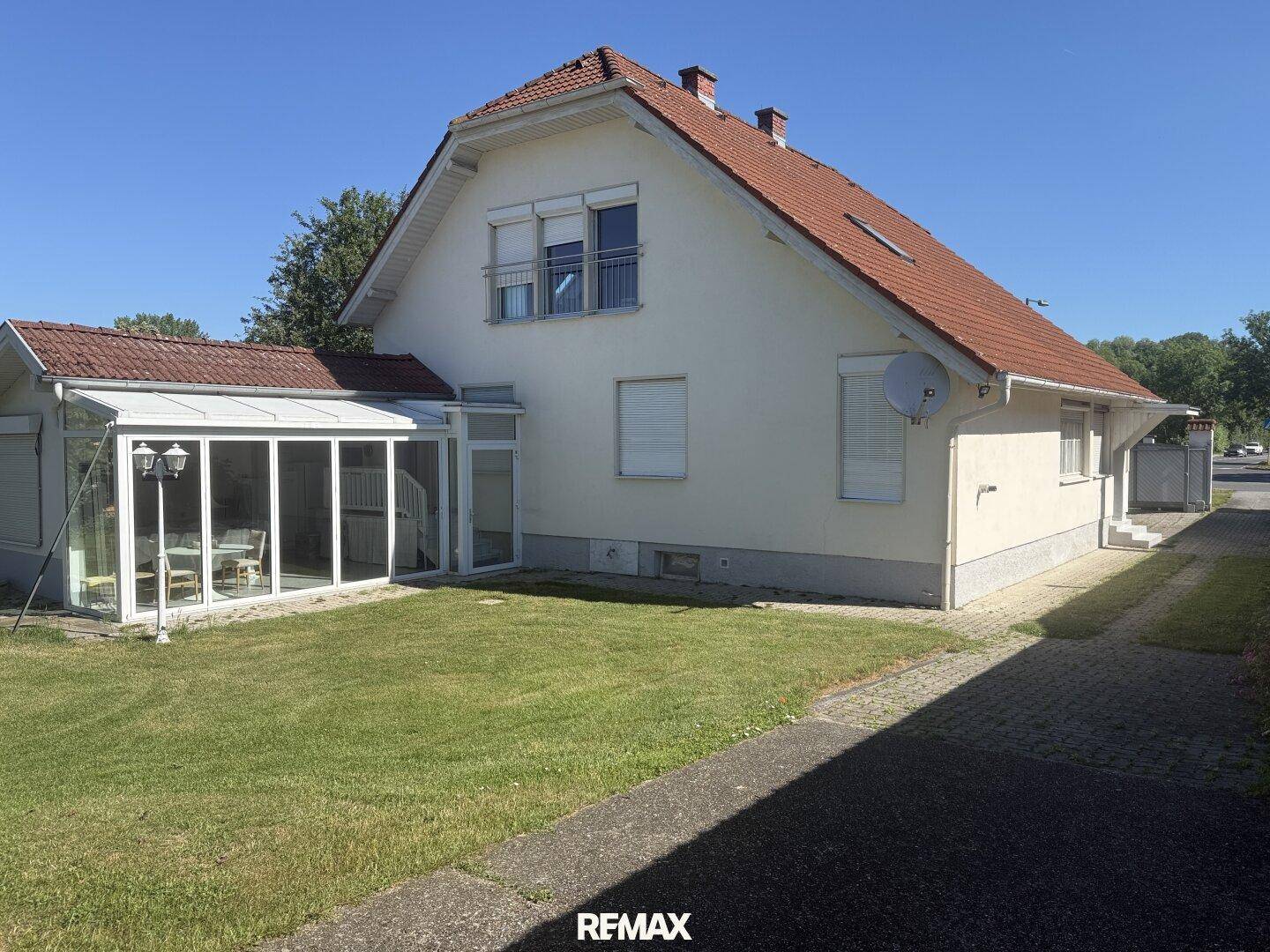 Rückseite des Hauses mit Wintergarten und gepflegtem Rasen unter strahlend blauem Himmel.