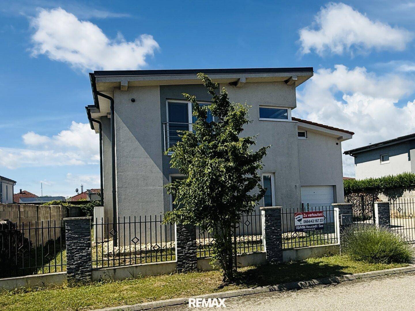Seitenansicht eines modernen Hauses mit Gartenbereich und Zaun unter blauem Himmel.