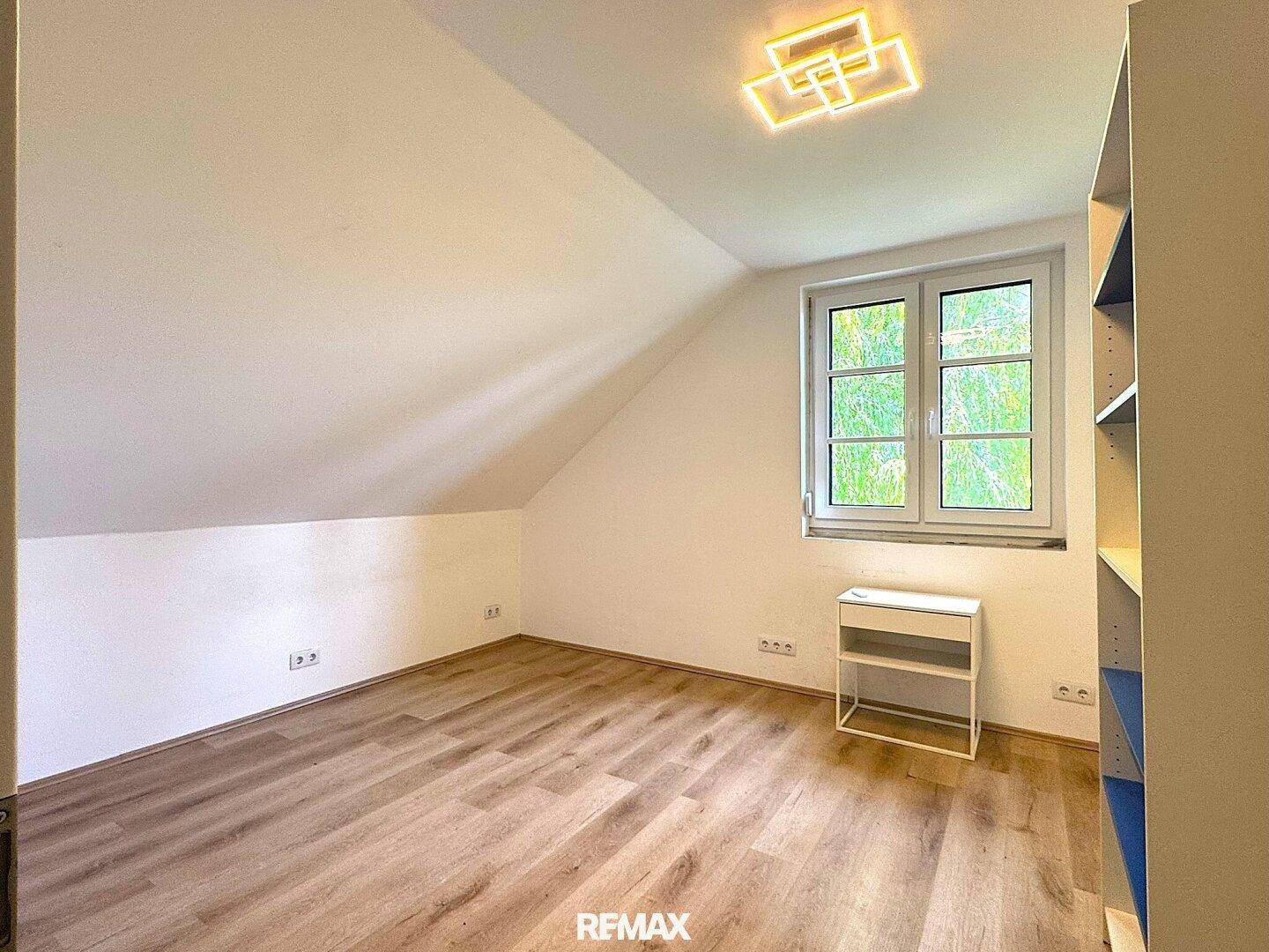 Freundliches Schlafzimmer im Dachgeschoss mit Laminatboden und einem großen Fenster.