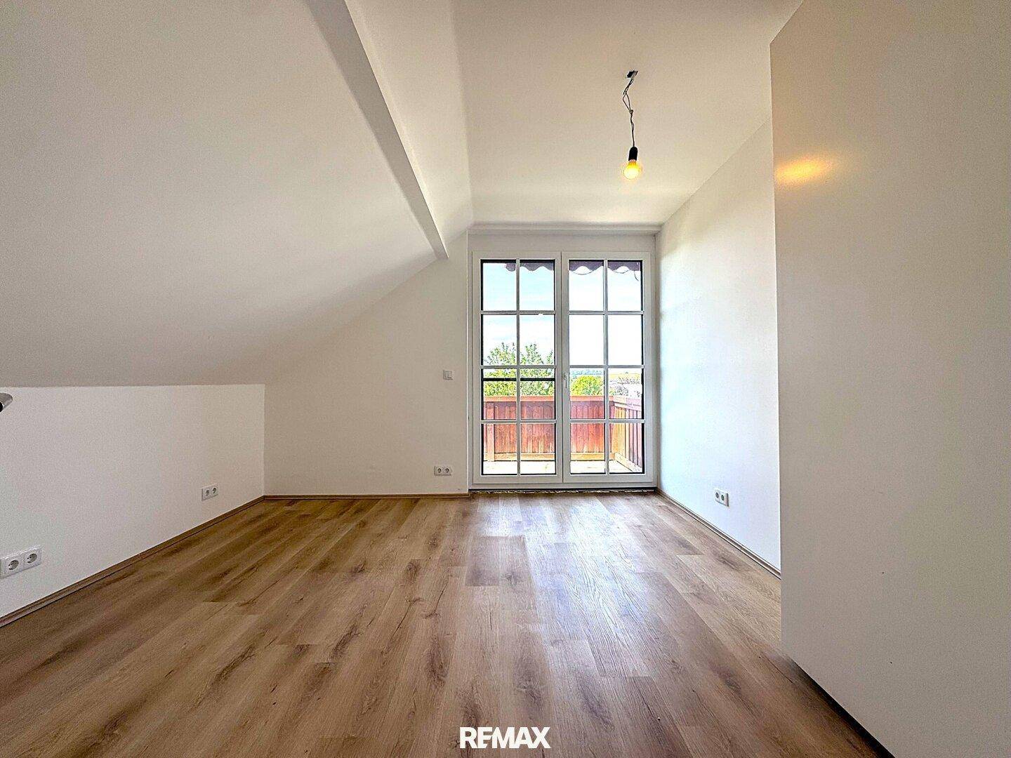 Geräumiges Schlafzimmer im Dachgeschoss mit Laminatboden und Zugang zu einem Balkon.