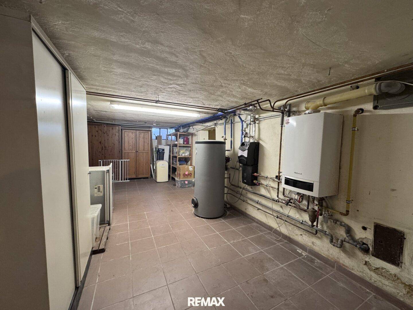 Technikraum im Keller mit Heizungsanlage, Warmwasserspeicher und Fliesenboden.
