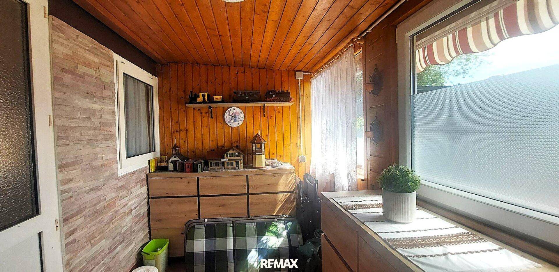 Helle Veranda mit Holzverkleidung, großen Fenstern und Blick ins Grüne.