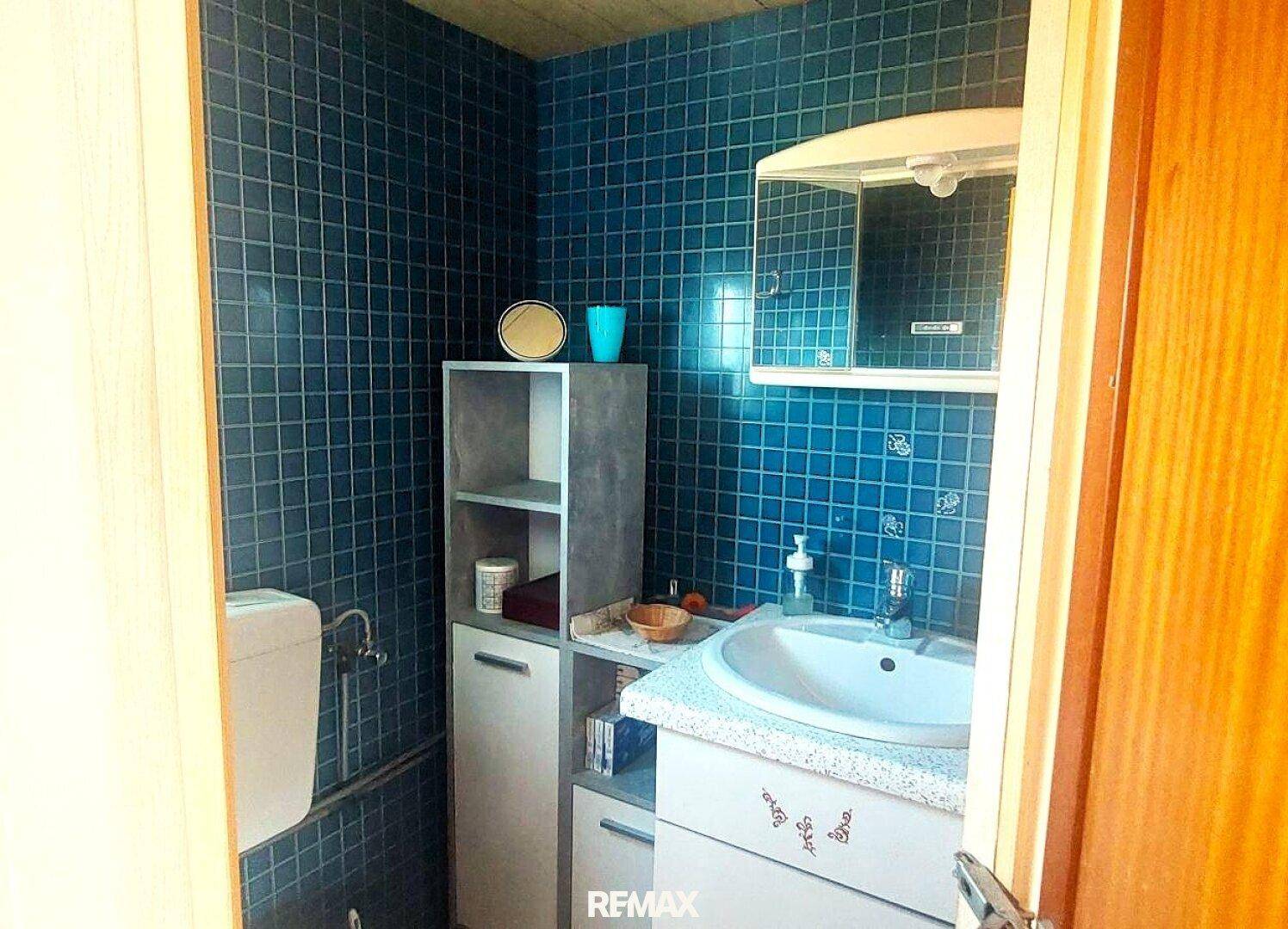 Kleines Badezimmer mit blauen Fliesen, Waschbecken und Spiegelschrank im 80er-Jahre-Stil.