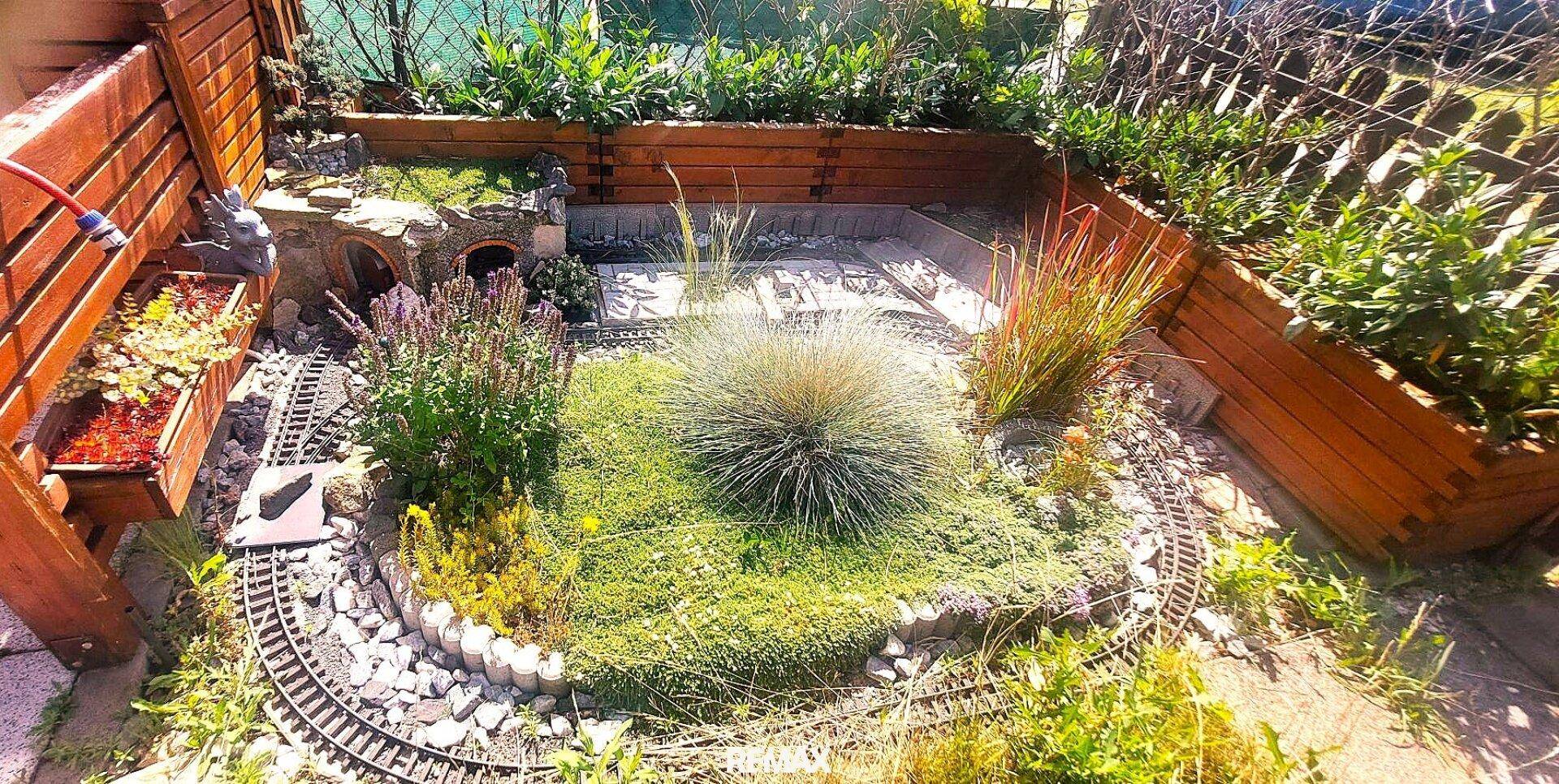 Kreativ gestalteter Gartenbereich mit Pflanzenbeeten, Steinen und einer Modelleisenbahn.