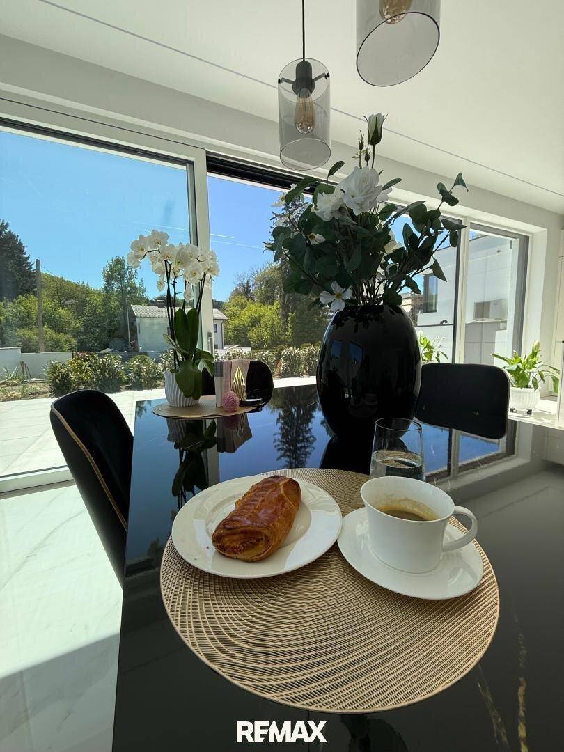 Detailaufnahme des Esstisches mit Frühstück und Blick durch die großen Fenster ins Grüne.