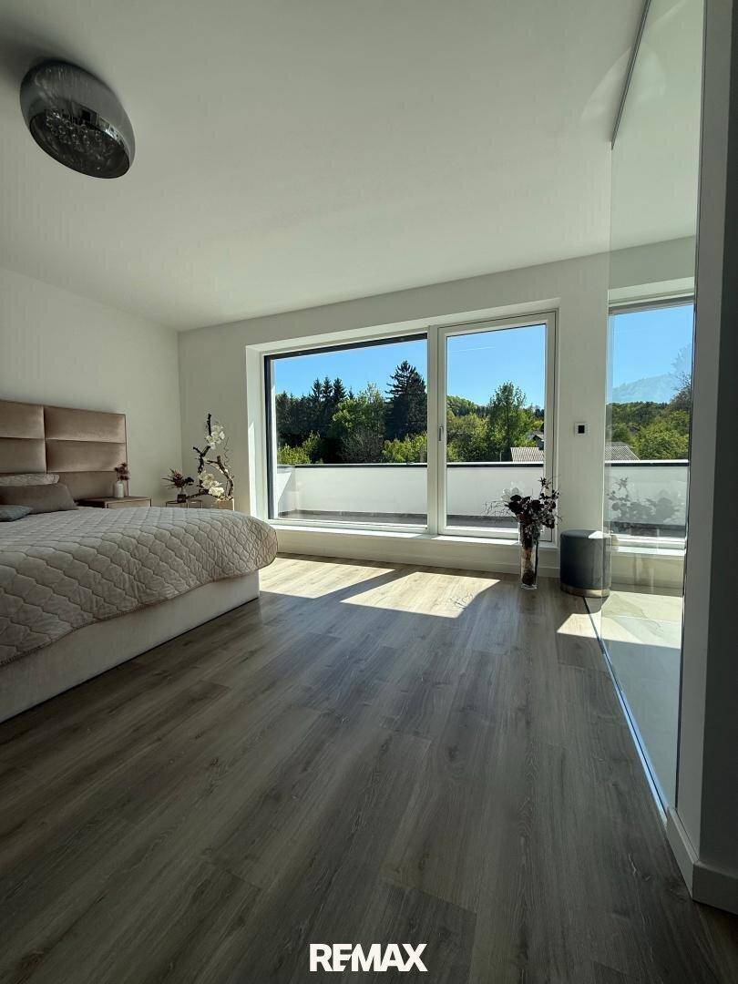 Helles Schlafzimmer mit großem Fenster, das einen schönen Blick ins Grüne bietet.