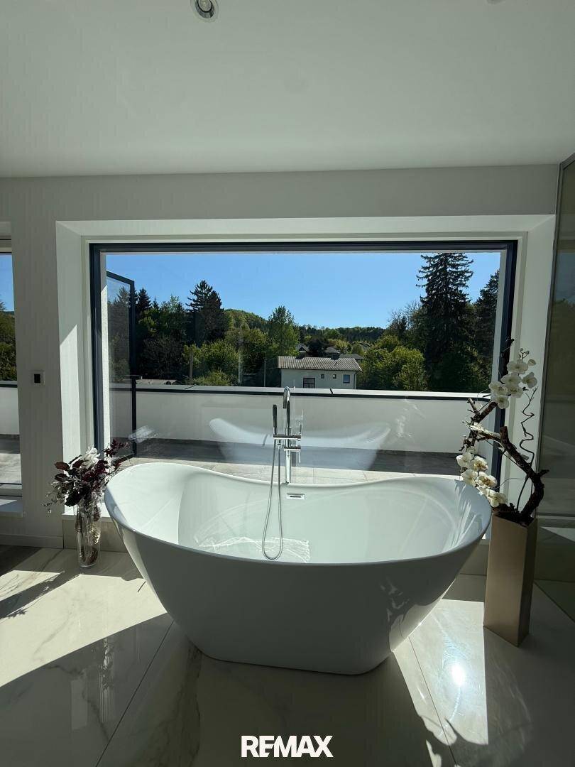 Elegantes Badezimmer mit freistehender Badewanne und Panoramafenster mit Blick ins Grüne.