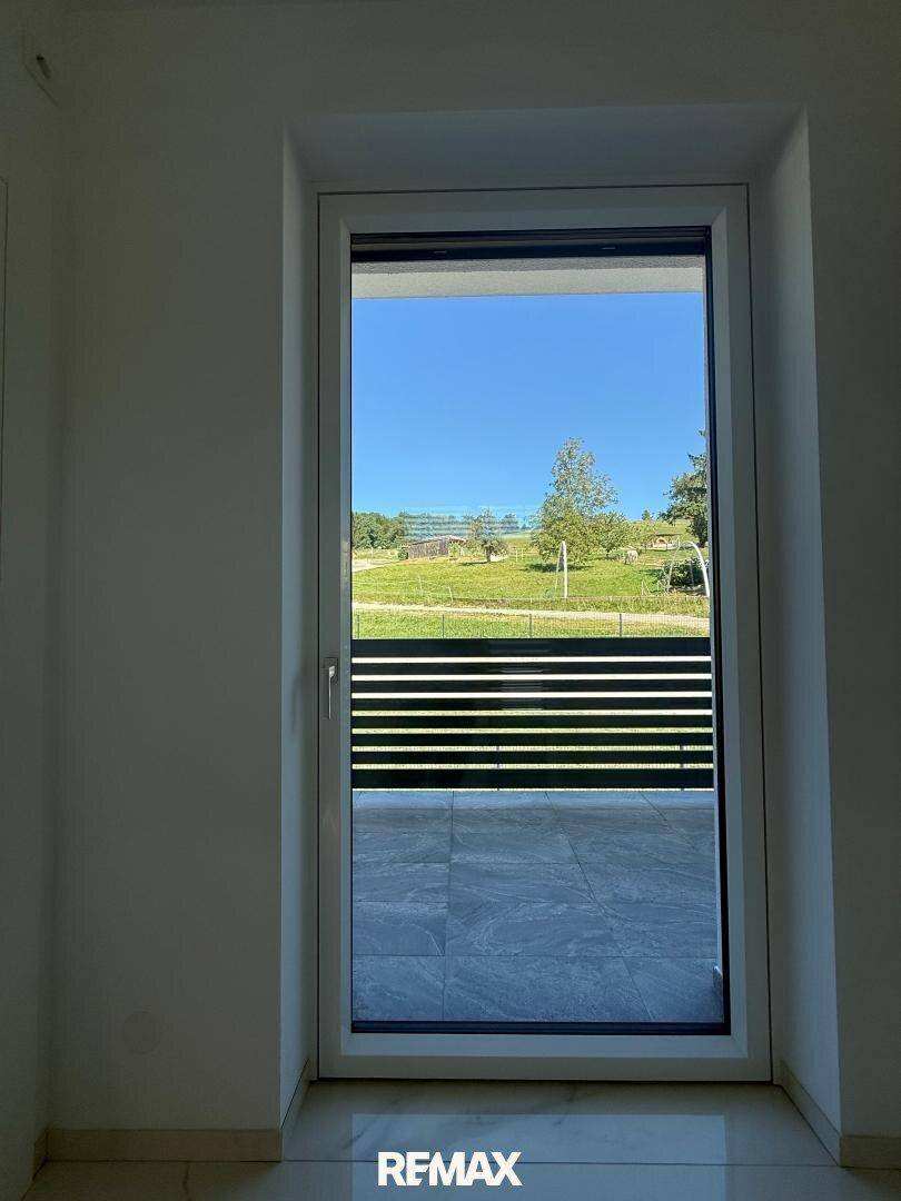 Fenster mit Blick auf eine grüne Wiese und den blauen Himmel, mit Rollladen.