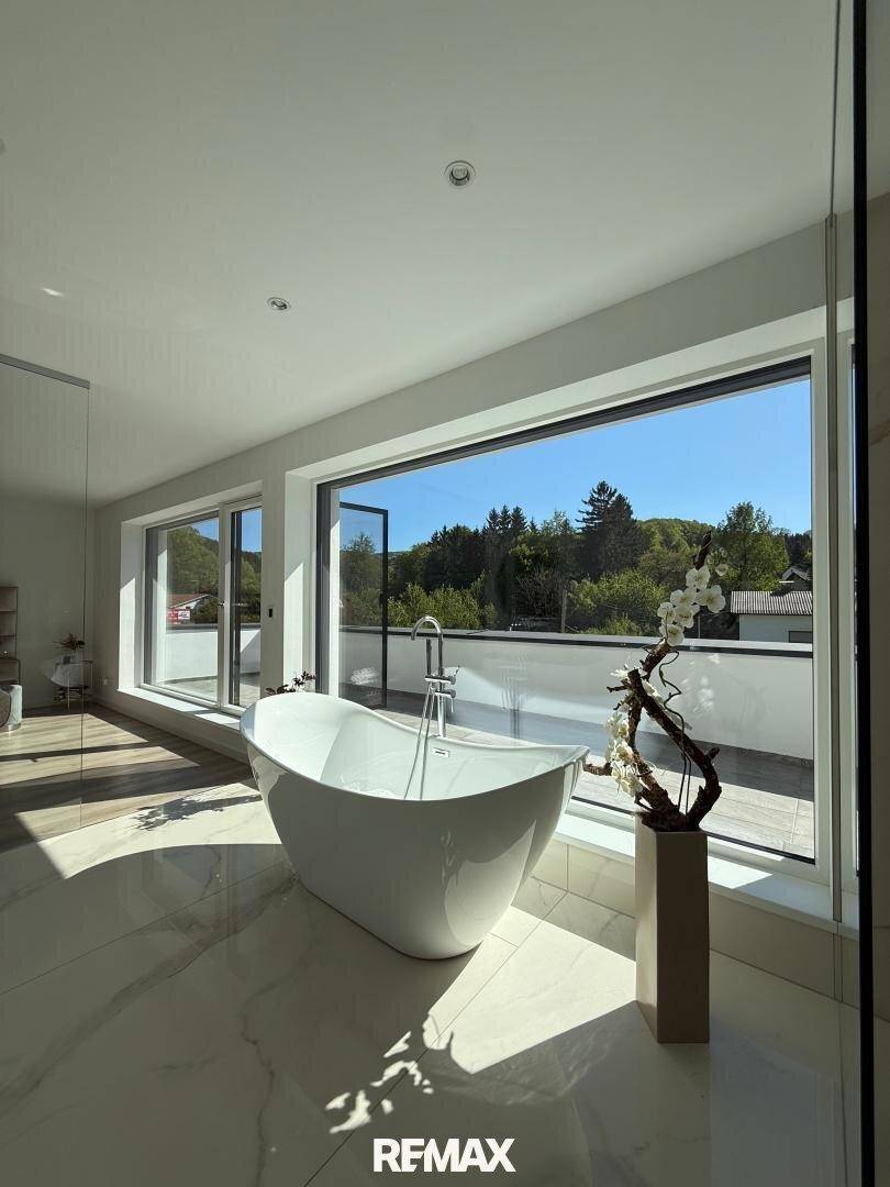 Lichtdurchflutetes Badezimmer mit freistehender Badewanne und weitem Blick in die Natur.