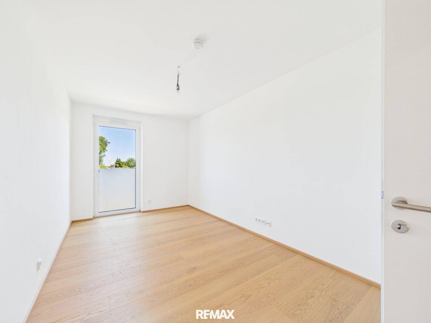 Helles Zimmer mit Holzparkett und Zugang zu einem französischen Balkon.