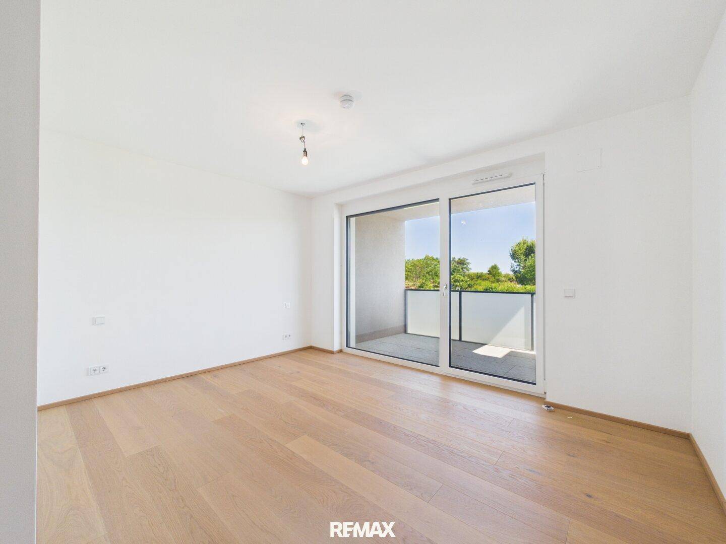 Helles Zimmer mit Holzparkett und großem Schiebefenster zum Balkon.