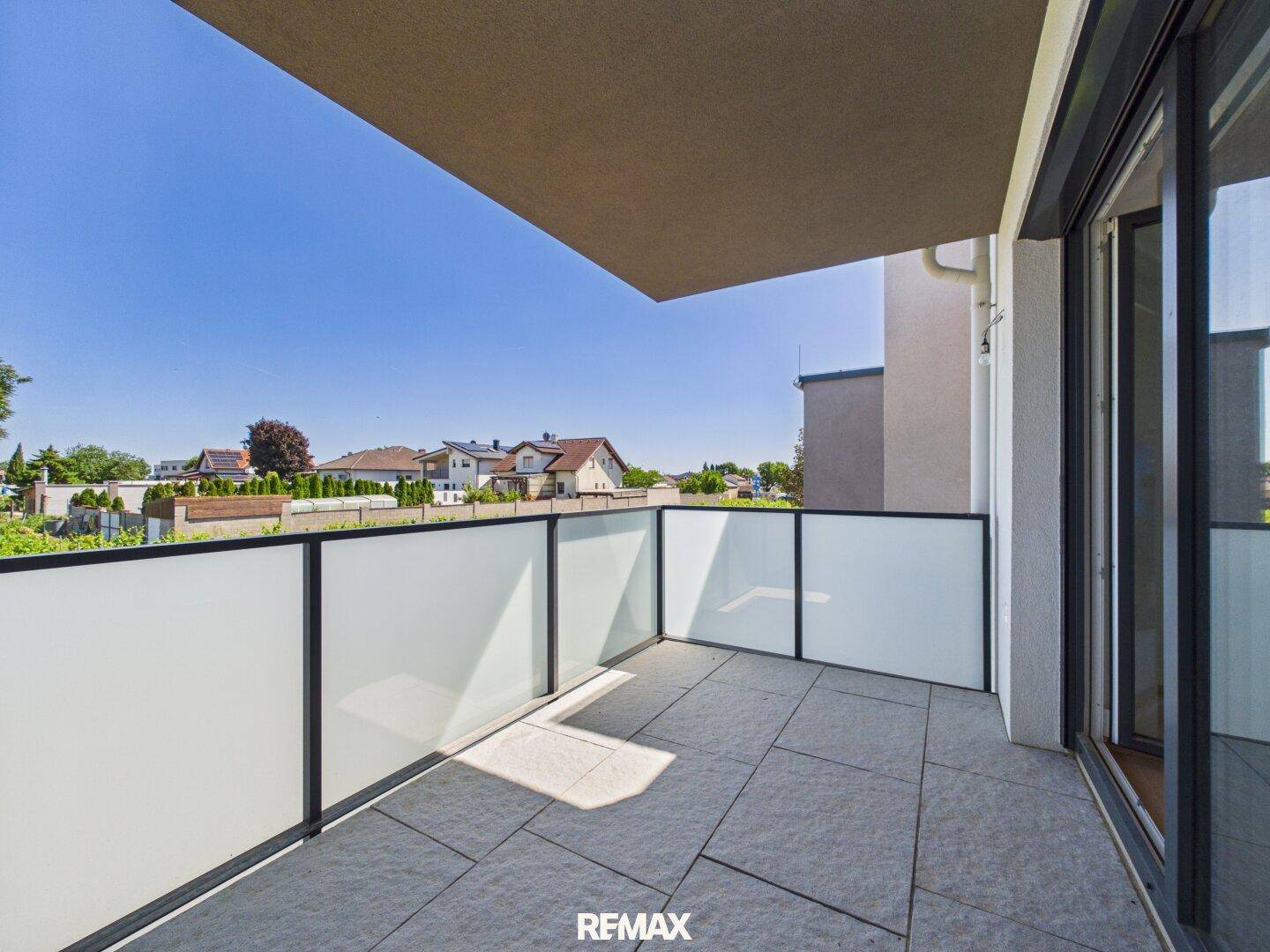 Geräumiger Balkon mit Fliesenboden und moderner Glasbrüstung mit Blick auf die Umgebung.