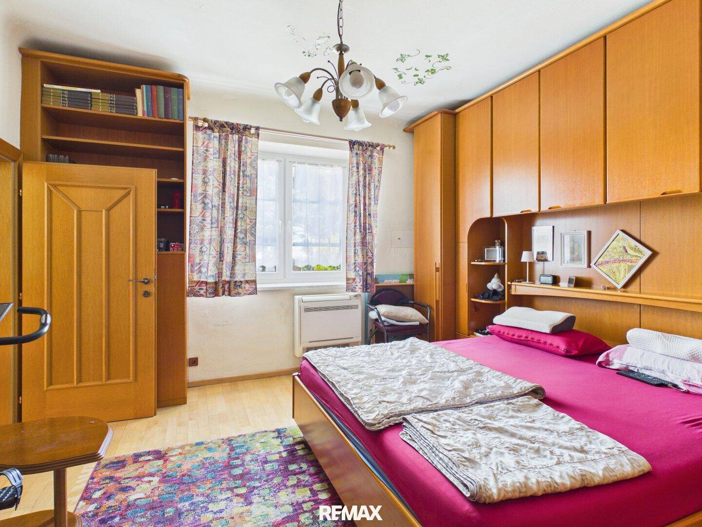 Schlafzimmer mit großem Bett, integrierten Holzschränken und einem Fenster mit Vorhängen.