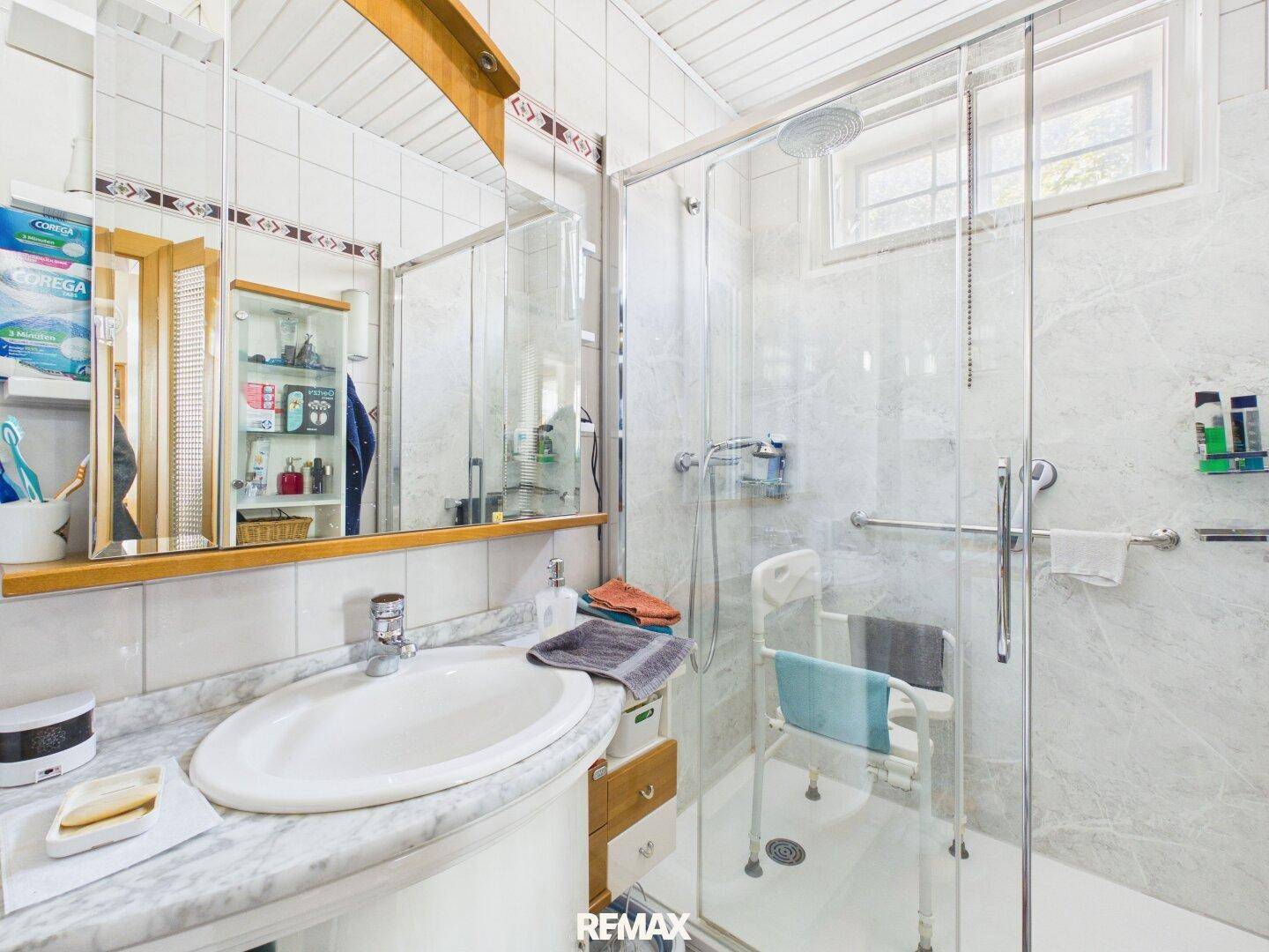 Helles Badezimmer mit barrierefreier Dusche, einzelnen Waschbecken und Spiegelschrank.