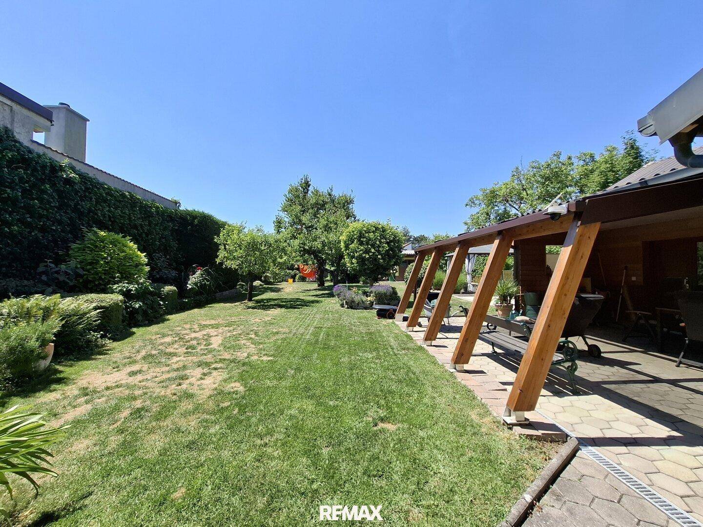 Langer Gartenbereich neben der überdachten Terrasse, umgeben von viel Grün und Bäumen.