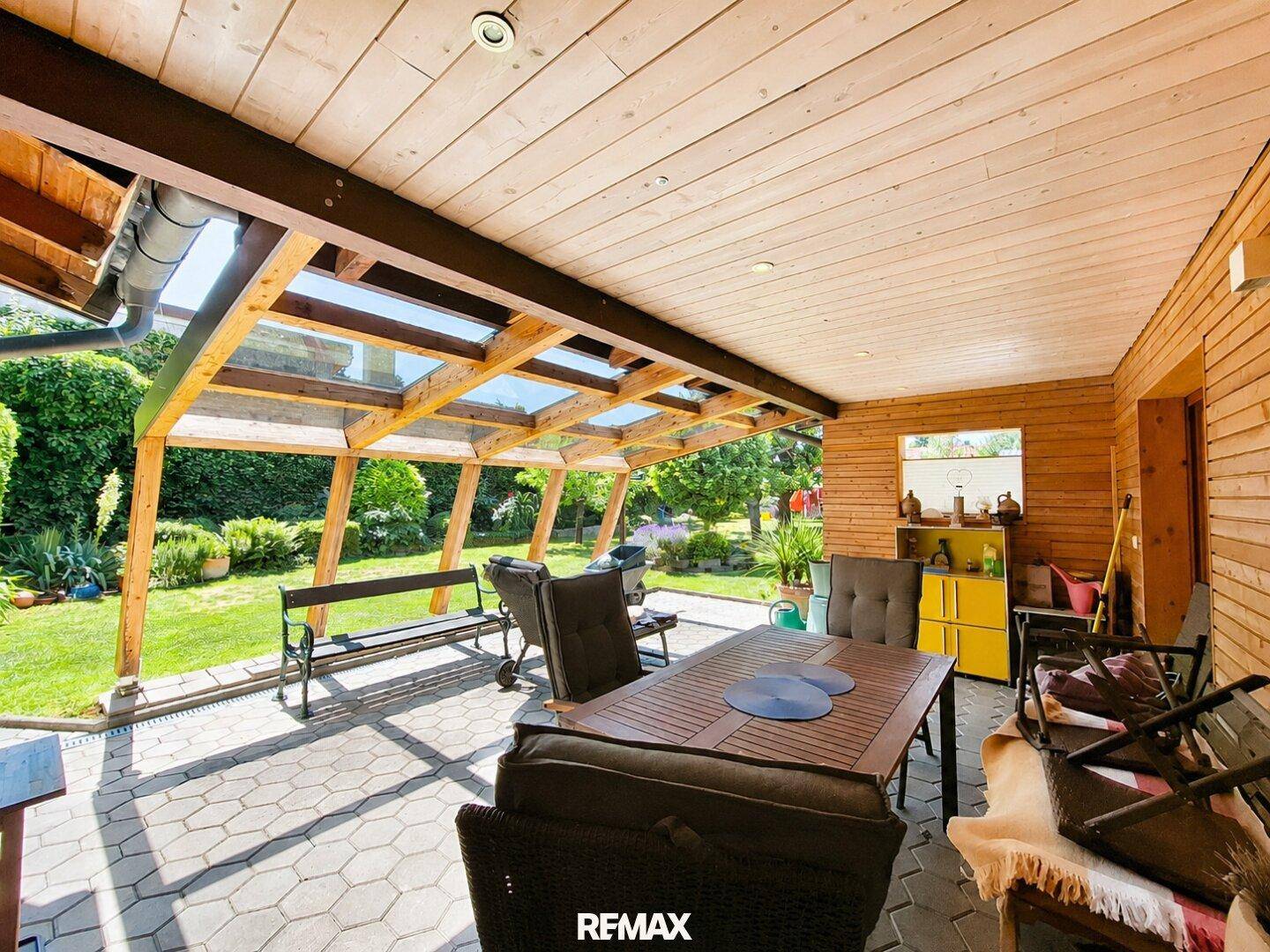 Gemütliche, überdachte Terrasse mit Holzdach, Esstisch und Blick ins Grüne.