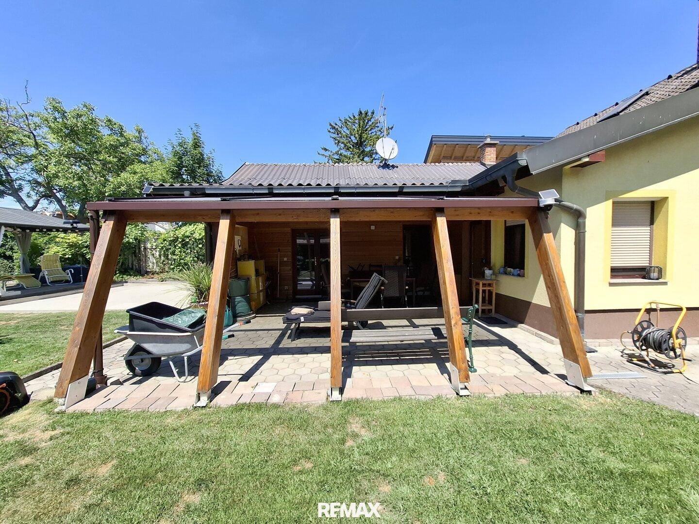 Überdachte Terrasse mit Holzbalken und gepflastertem Boden, Blick in den Garten.