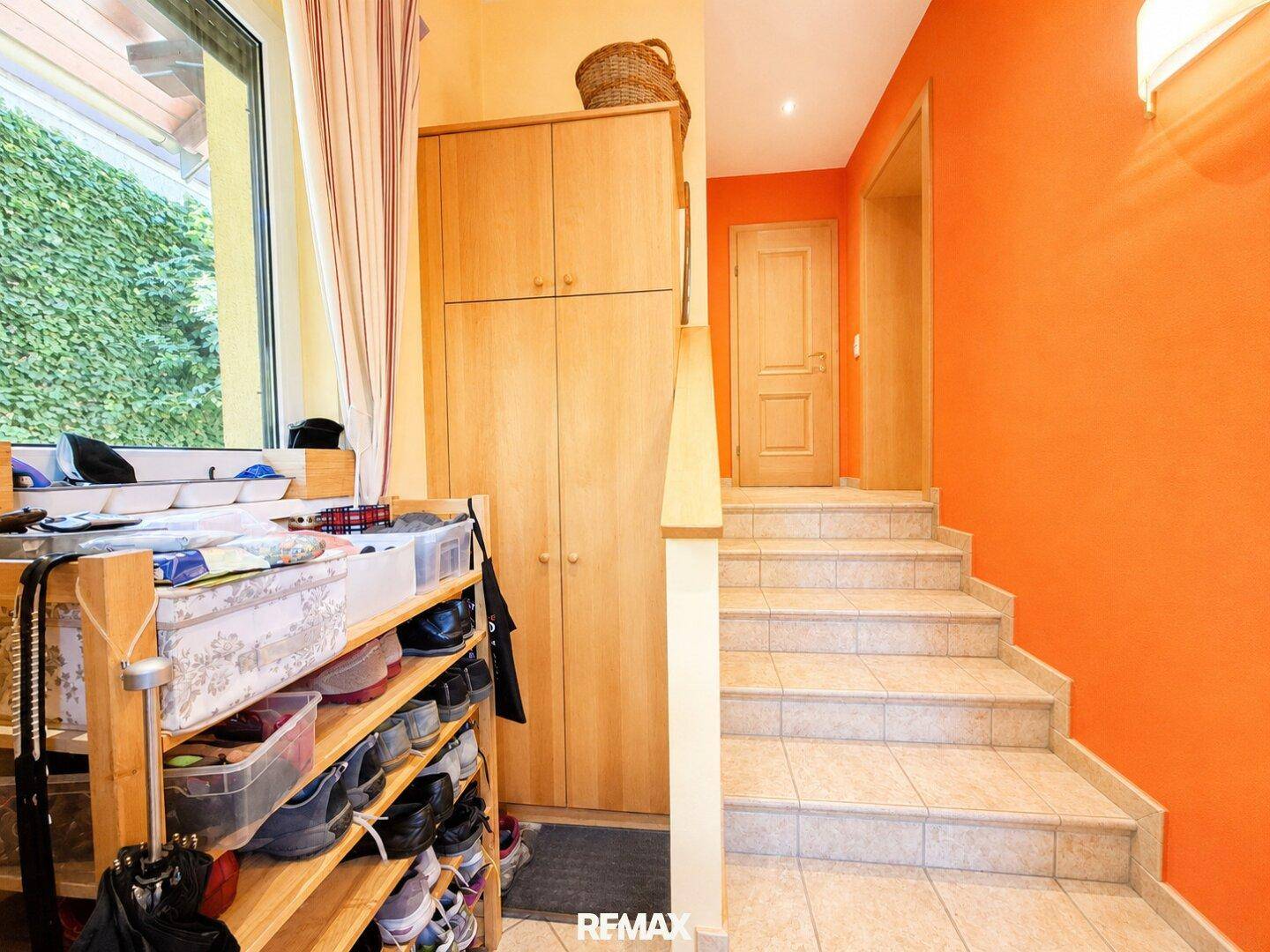 Heller Flur mit orangefarbenen Wänden, Holzschrank und Treppe zum Obergeschoss.