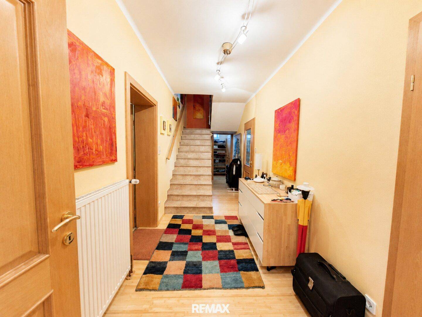 Geräumiger Flur mit Treppe, bunten Teppichen und hellen Wänden.