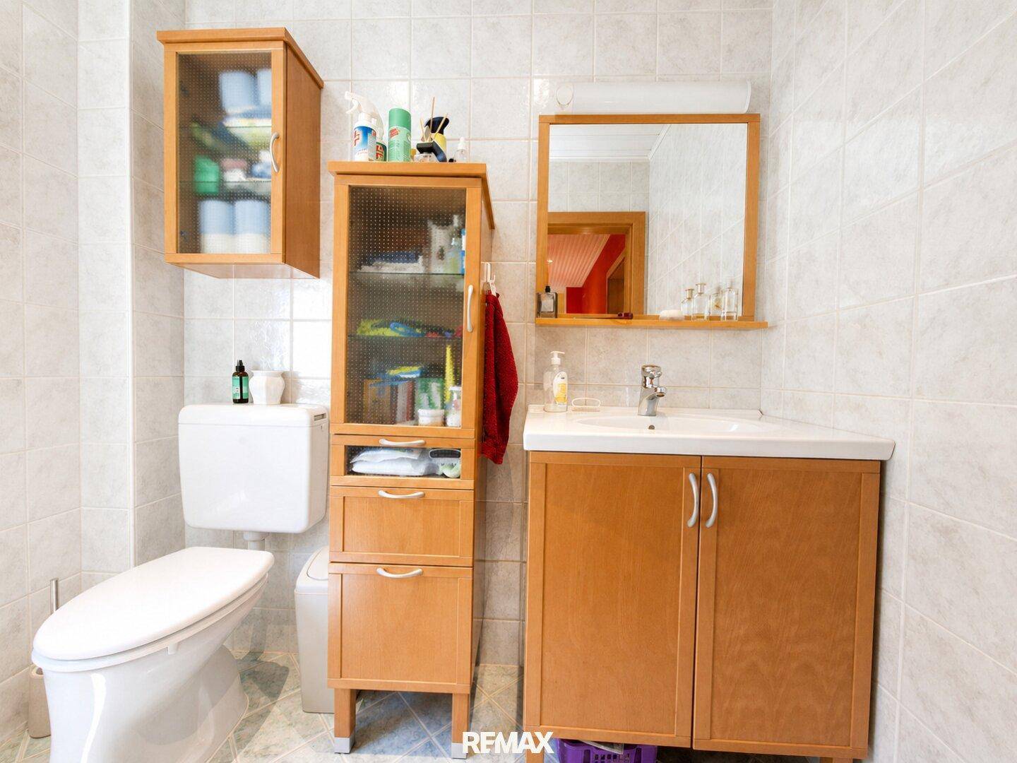 Kleines Badezimmer mit hellen Fliesen, WC, Waschbecken und Holzschränken.