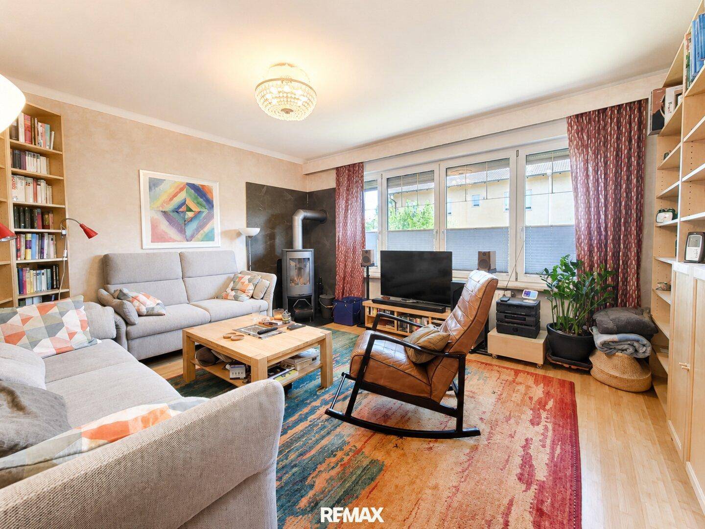 Geräumiges Wohnzimmer mit Kaminofen, bequemen Sofas und großem Fenster.