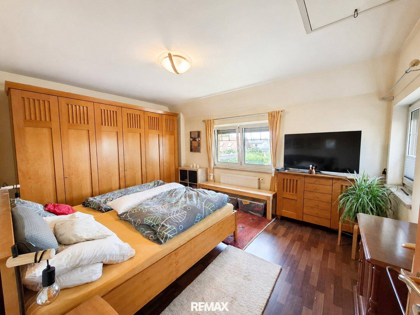 Geräumiges Schlafzimmer mit großem Holzkleiderschrank, Doppelbett und dunklem Laminatboden.