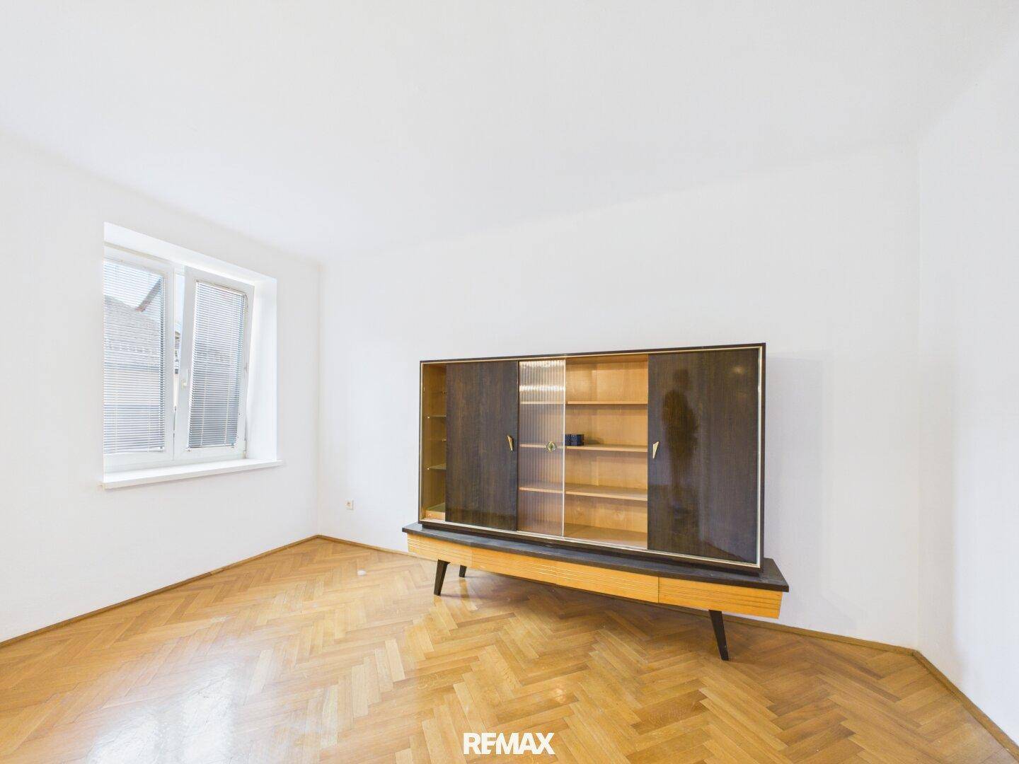 Geräumiger Raum mit klassischem Parkettboden und einem stilvollen Vintage-Sideboard unter dem Fenster.