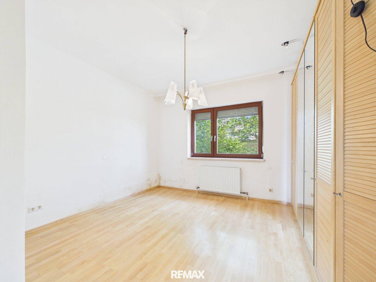 Helles Schlafzimmer mit Parkettboden, großem Fenster und Einbauschrank.