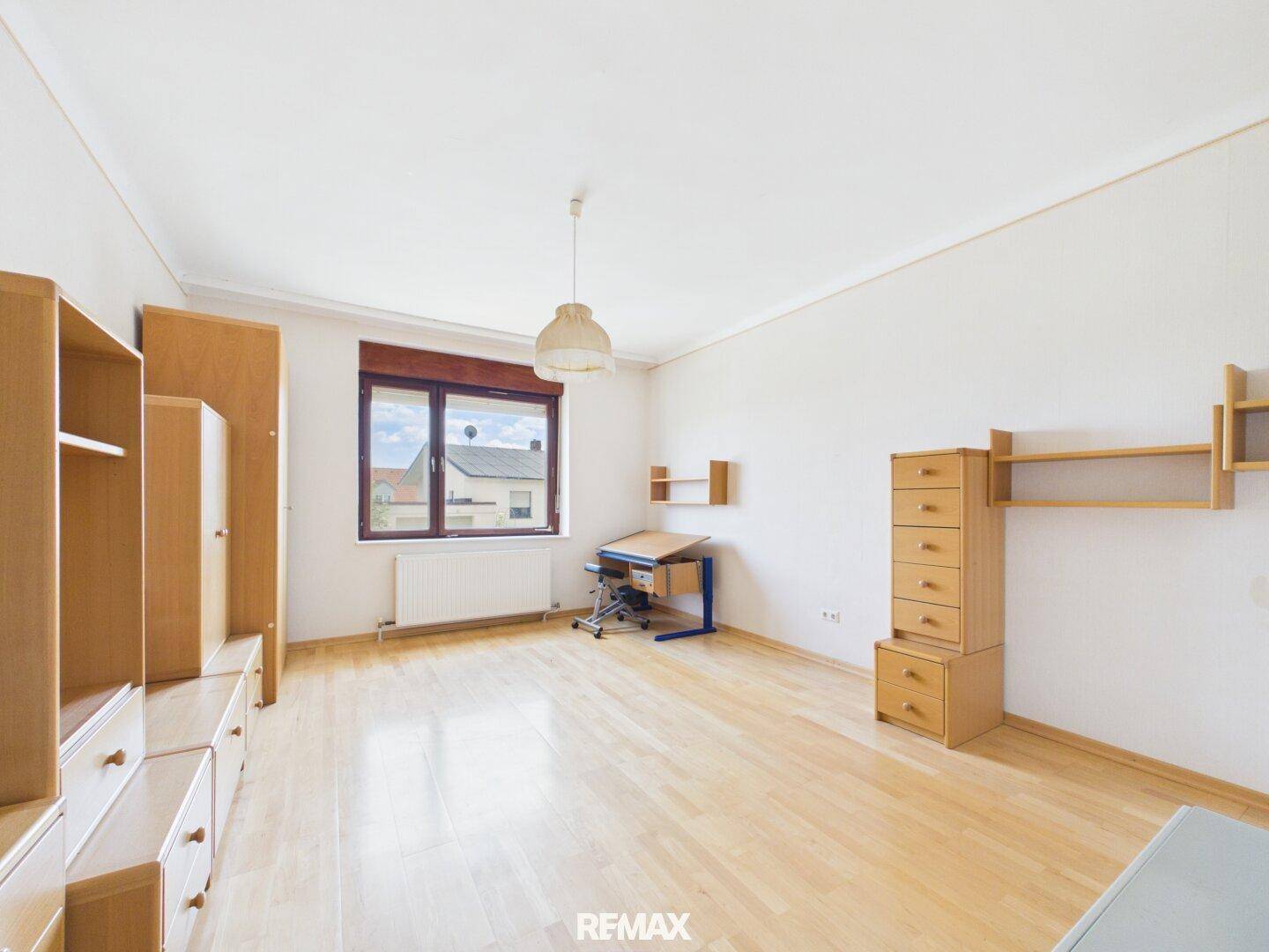 Helles Zimmer mit Parkettboden, großem Fenster und einfacher Einrichtung.