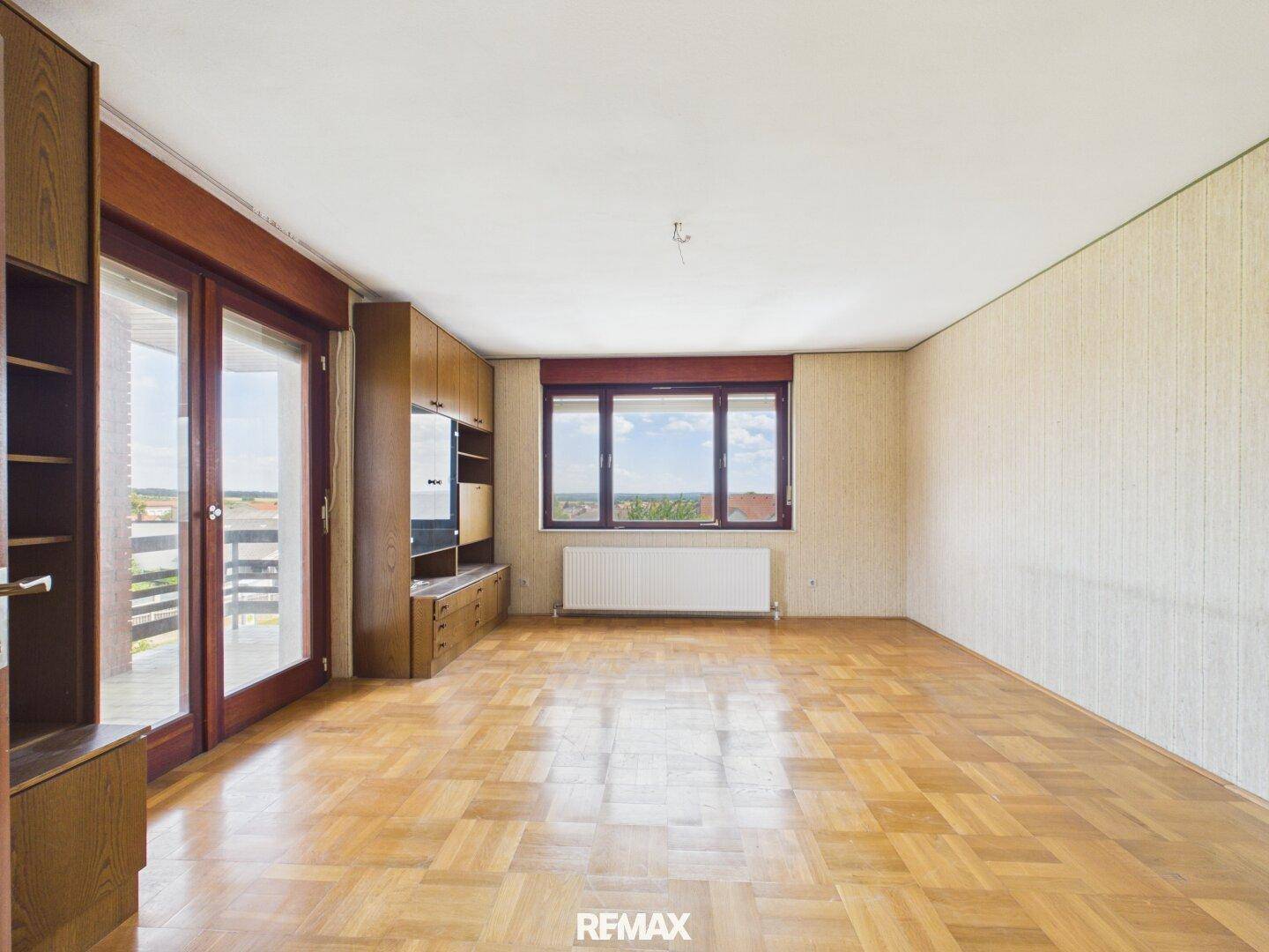 Geräumiges Wohnzimmer mit Parkettboden, Balkonzugang und weitem Ausblick.