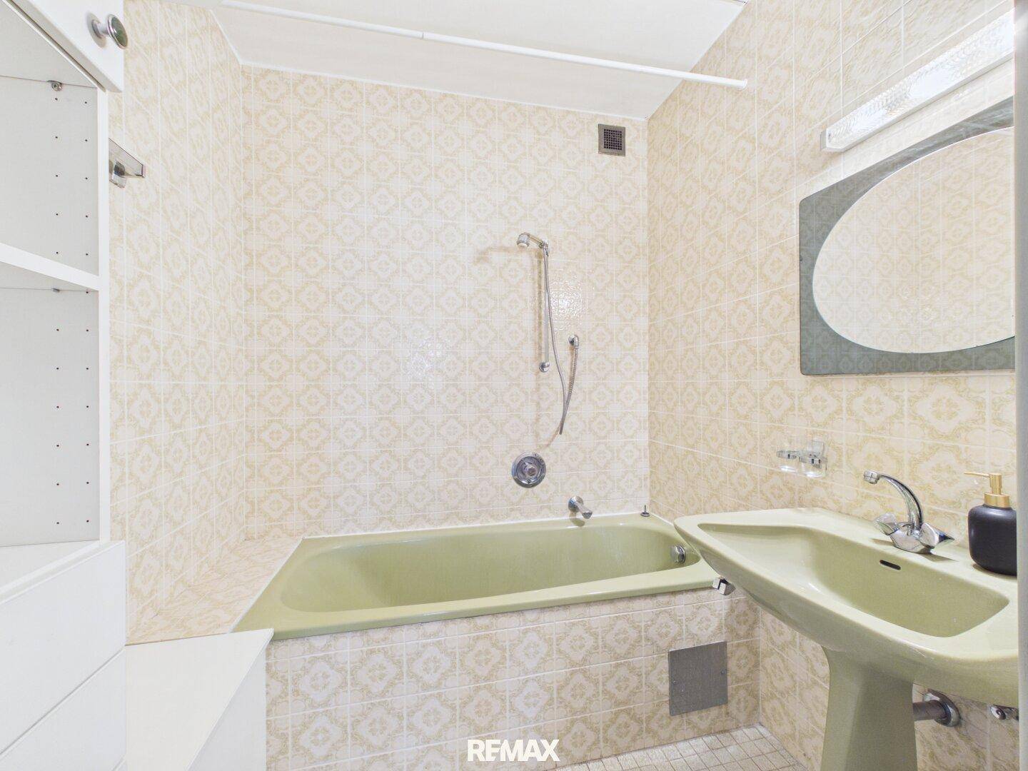 Badezimmer im 80er-Jahre-Stil mit grüner Badewanne und passendem Waschbecken.