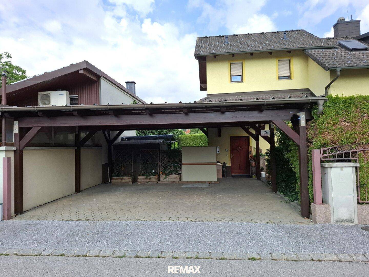 Vorderansicht des Hauses mit großem Carport und gepflasterter Einfahrt.