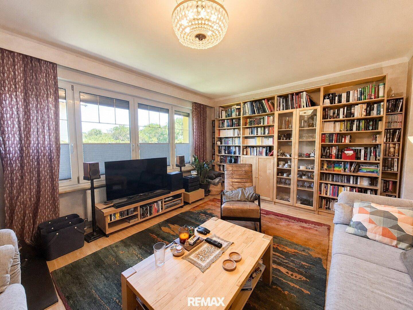 Helles Wohnzimmer mit umfangreichen Bücherregalen, Sofa und Blick ins Grüne.