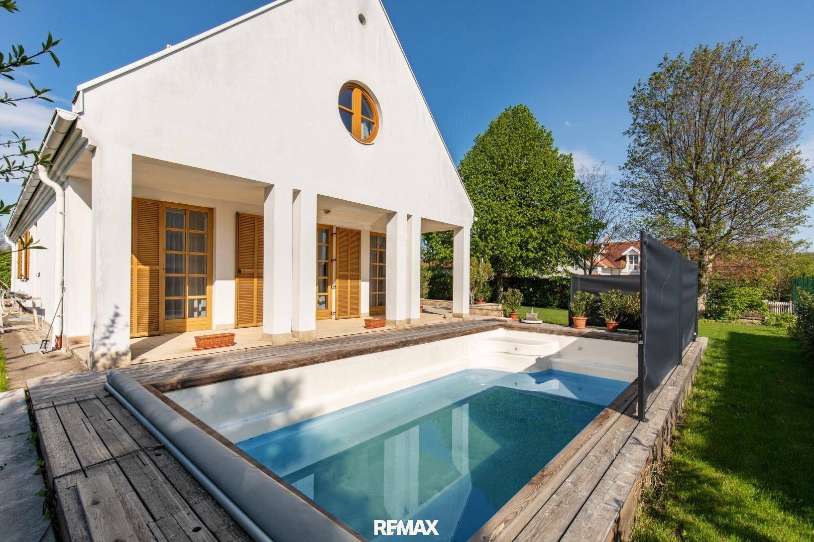 Außenansicht des Hauses mit eingelassenem Pool und Holzdeck im grünen Gartenbereich.