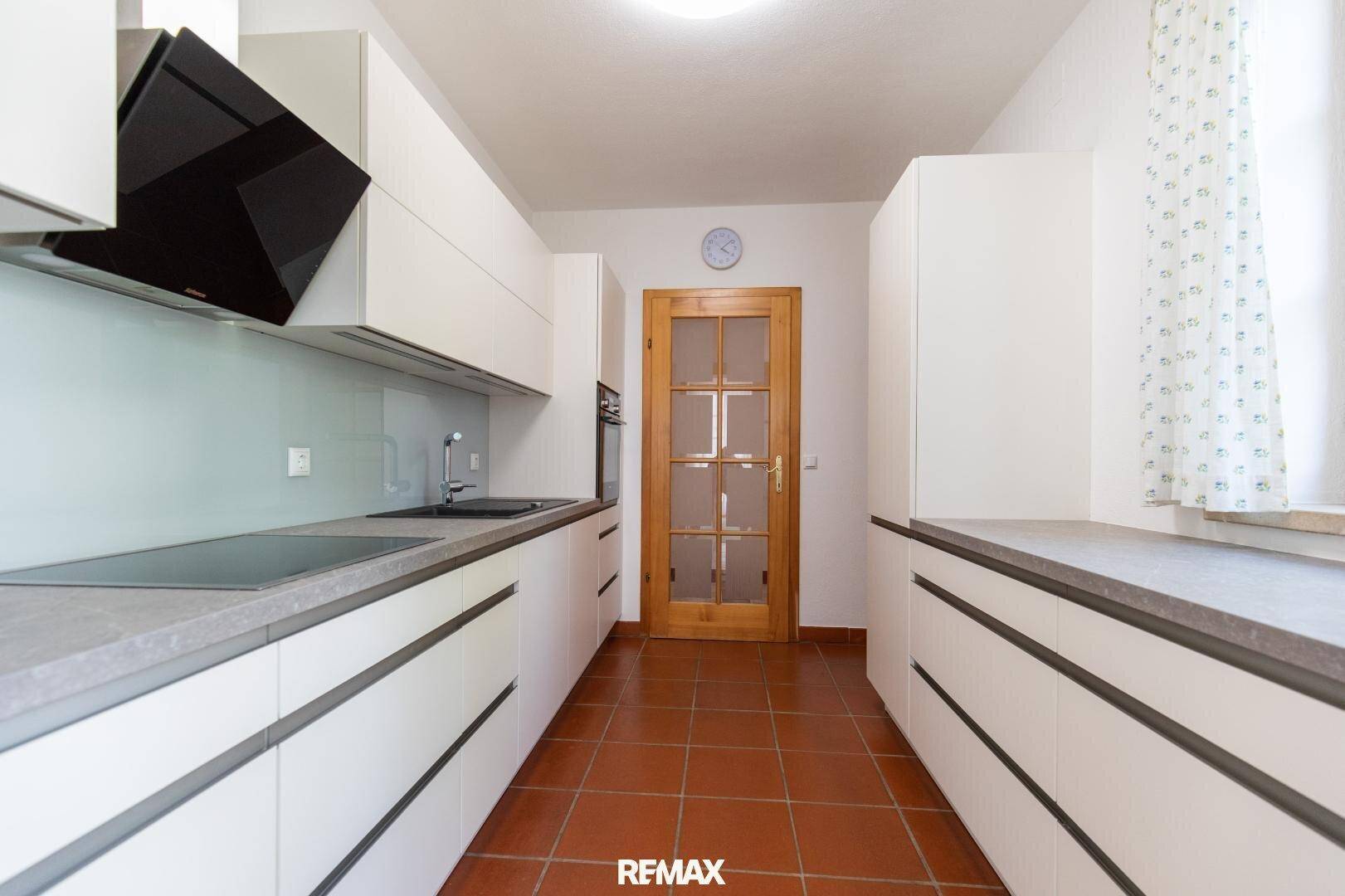 Moderne Küche mit weißen Schränken, dunkler Arbeitsplatte und Terrakottafliesen.