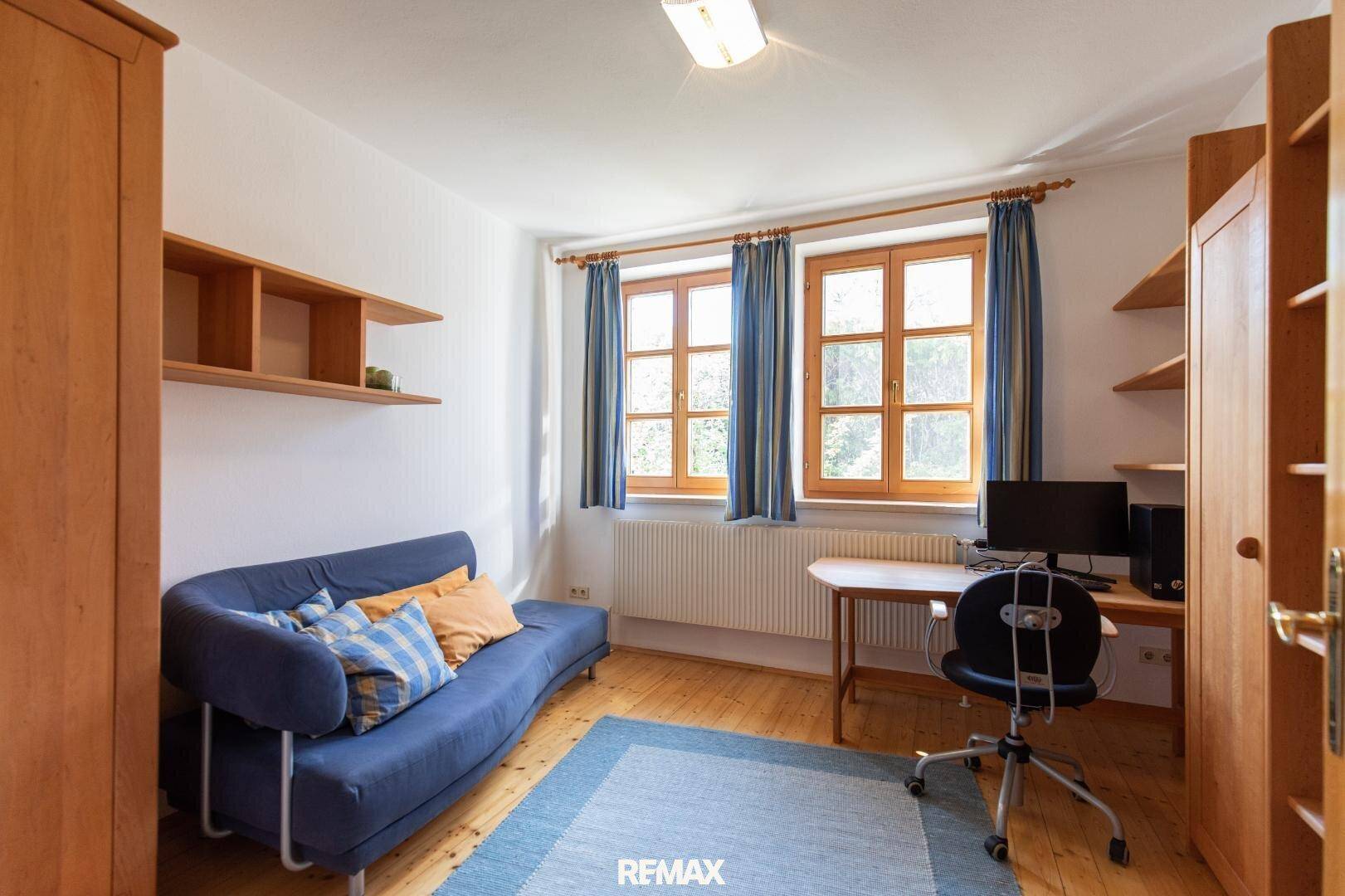 Helles Schlafzimmer mit Holzmöbeln, blauen Vorhängen und Blick ins Grüne.