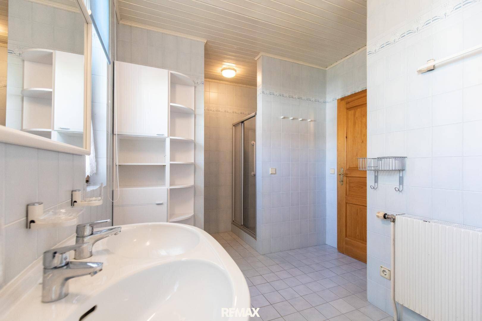 Badezimmer mit hellblauen Fliesen, Doppelwaschbecken und Duschkabine.