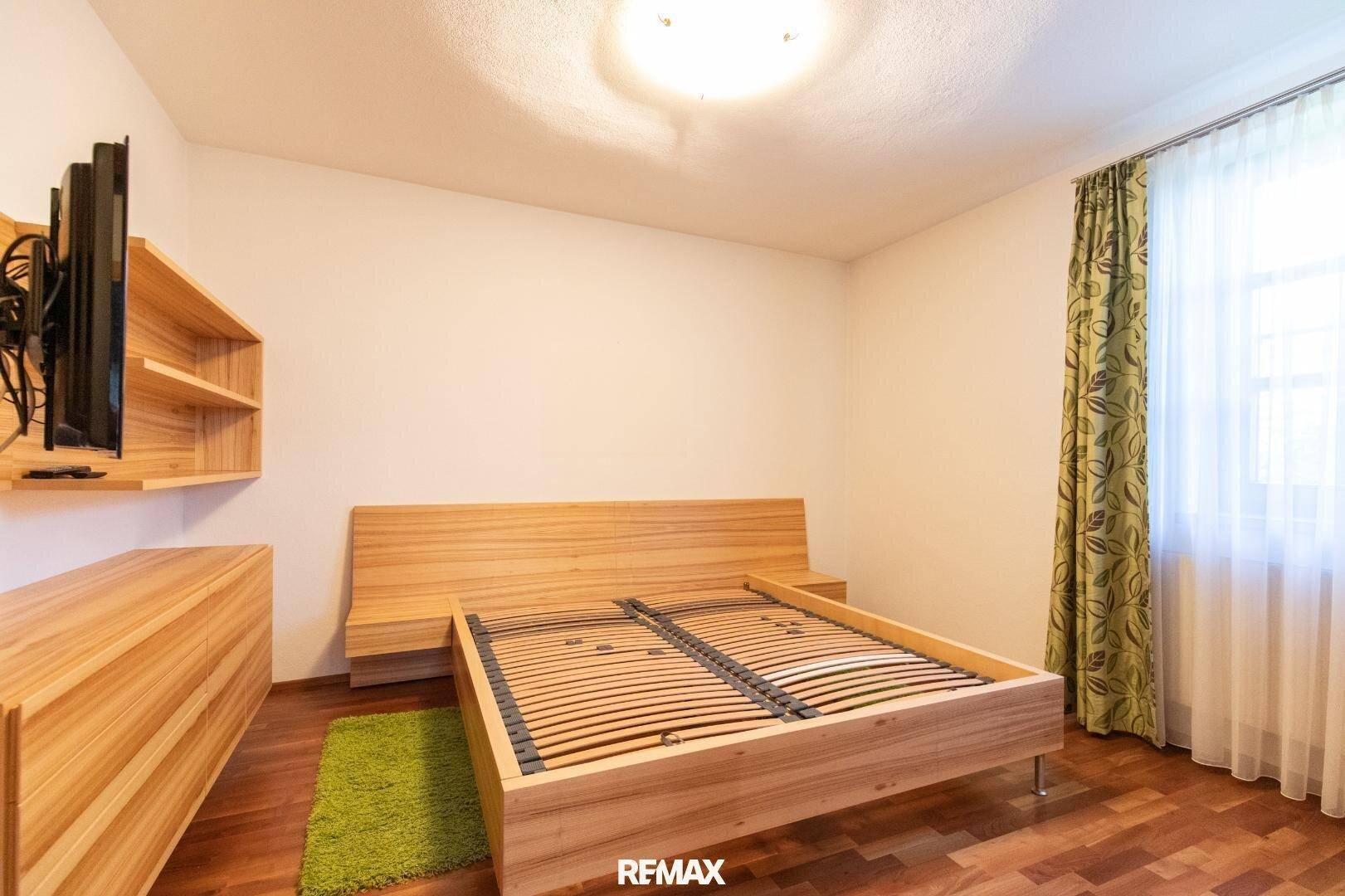 Schlafzimmer mit hellem Holzrahmenbett, Holzmöbeln und Parkettboden.