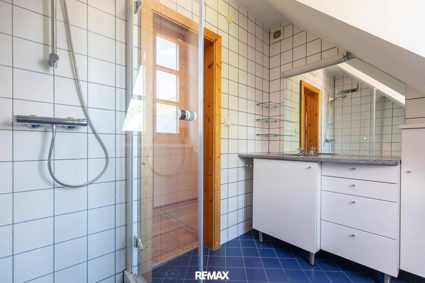 Badezimmer im Dachgeschoss mit Dusche, Waschtisch und blauen Bodenfliesen.