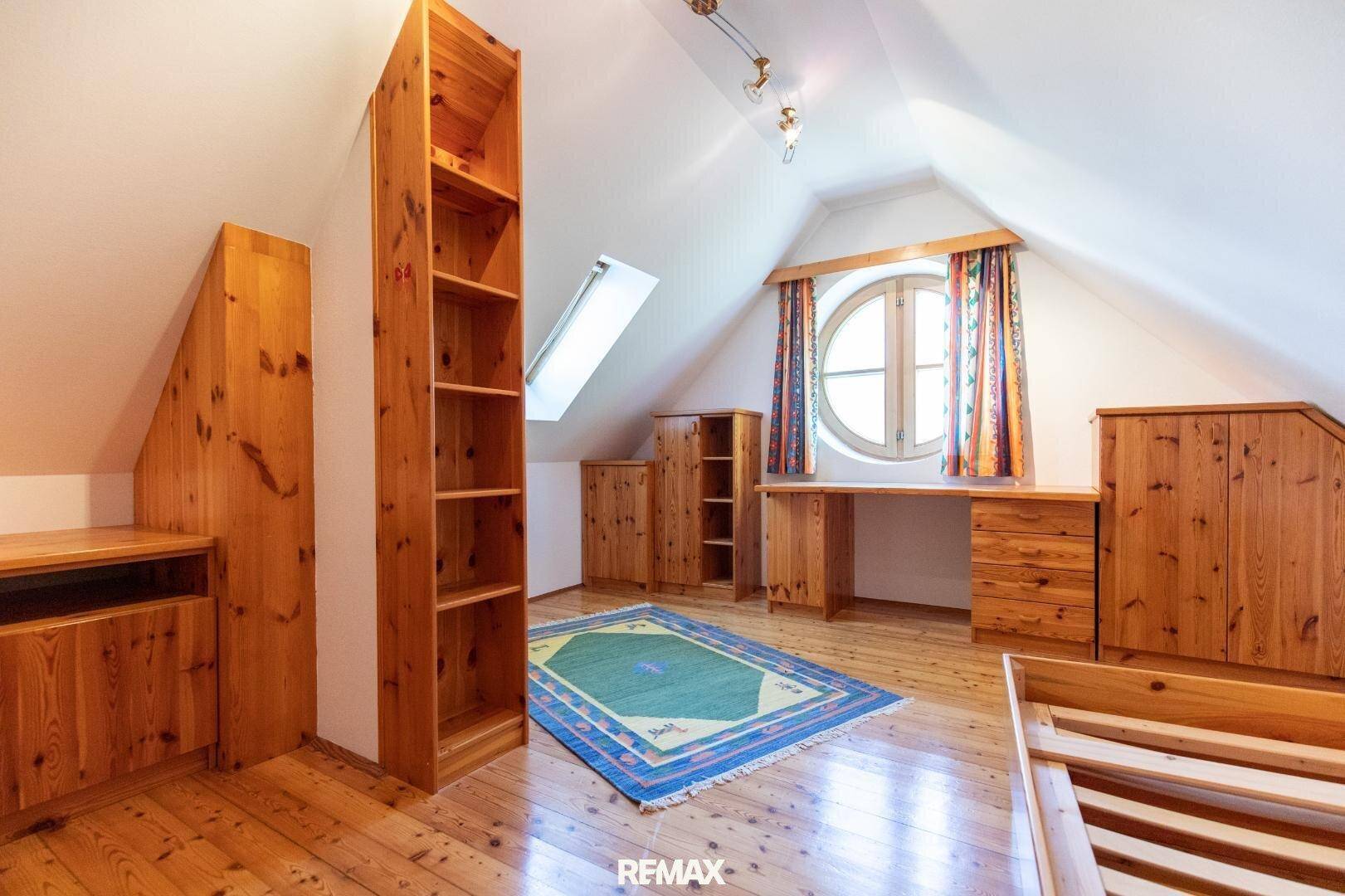 Helles Dachzimmer mit Holzboden, runden Fenstern und Einbauschränken.
